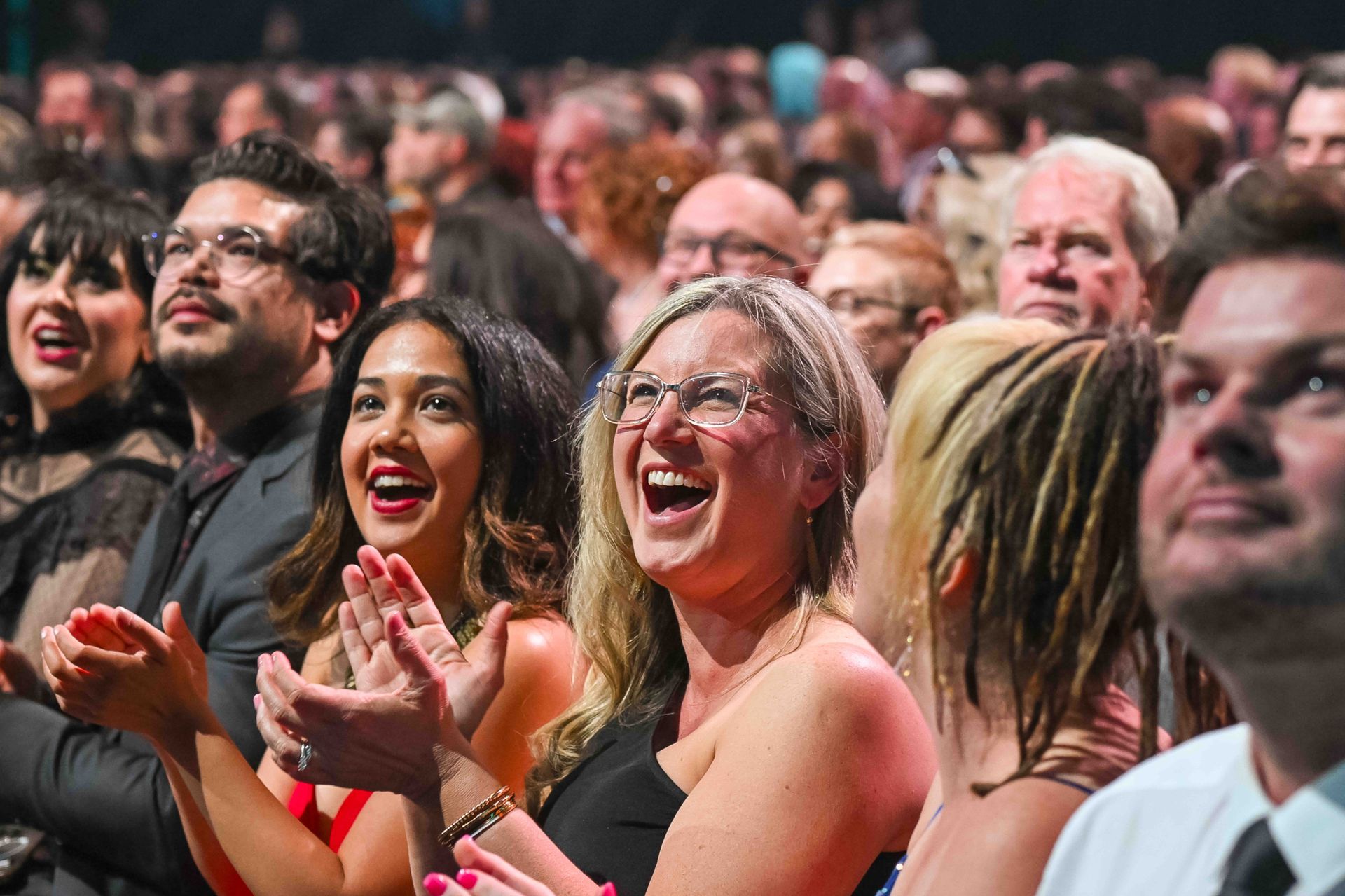 Woman in African print dress holds award, smiling. Man in suit smiles beside her. Stage setting.
