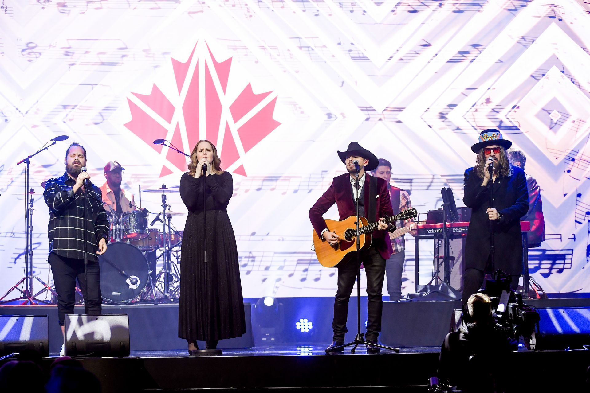 A group of people are standing on a stage singing into microphones.