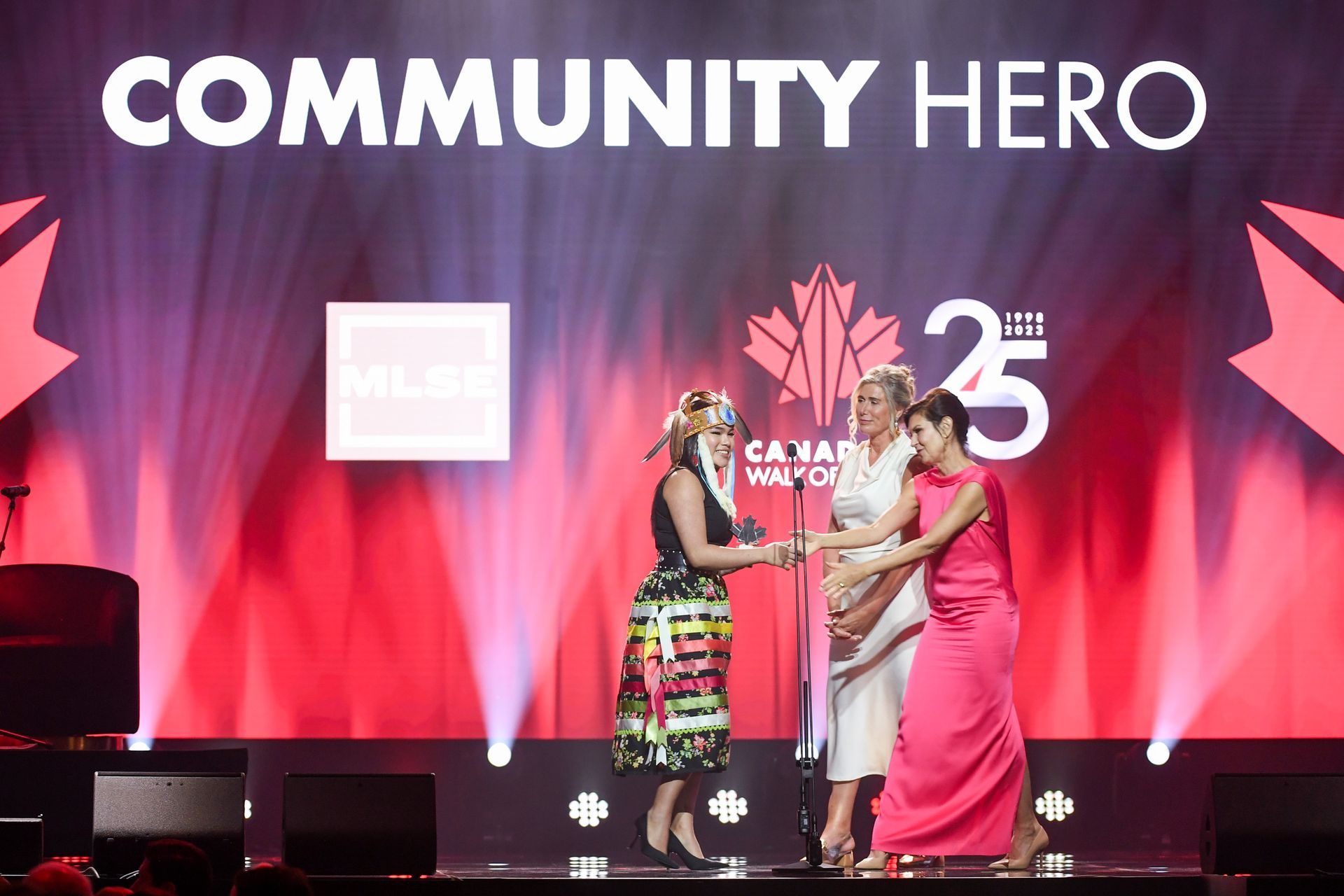 Three women are standing on a stage in front of a sign that says community hero.