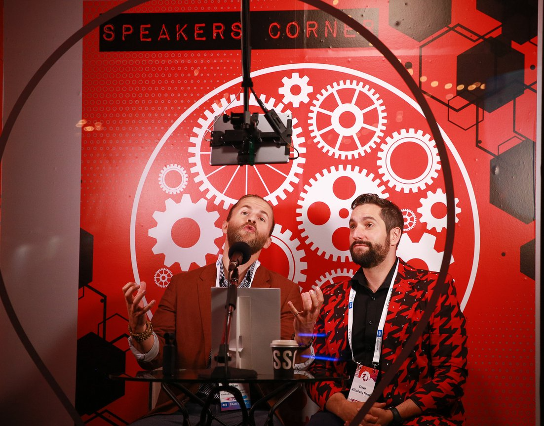 Two men are sitting in front of a microphone in a speakers corner.