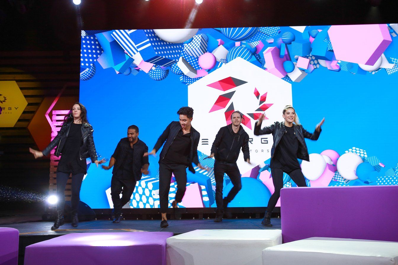 A group of men are dancing on a stage in front of a large screen.