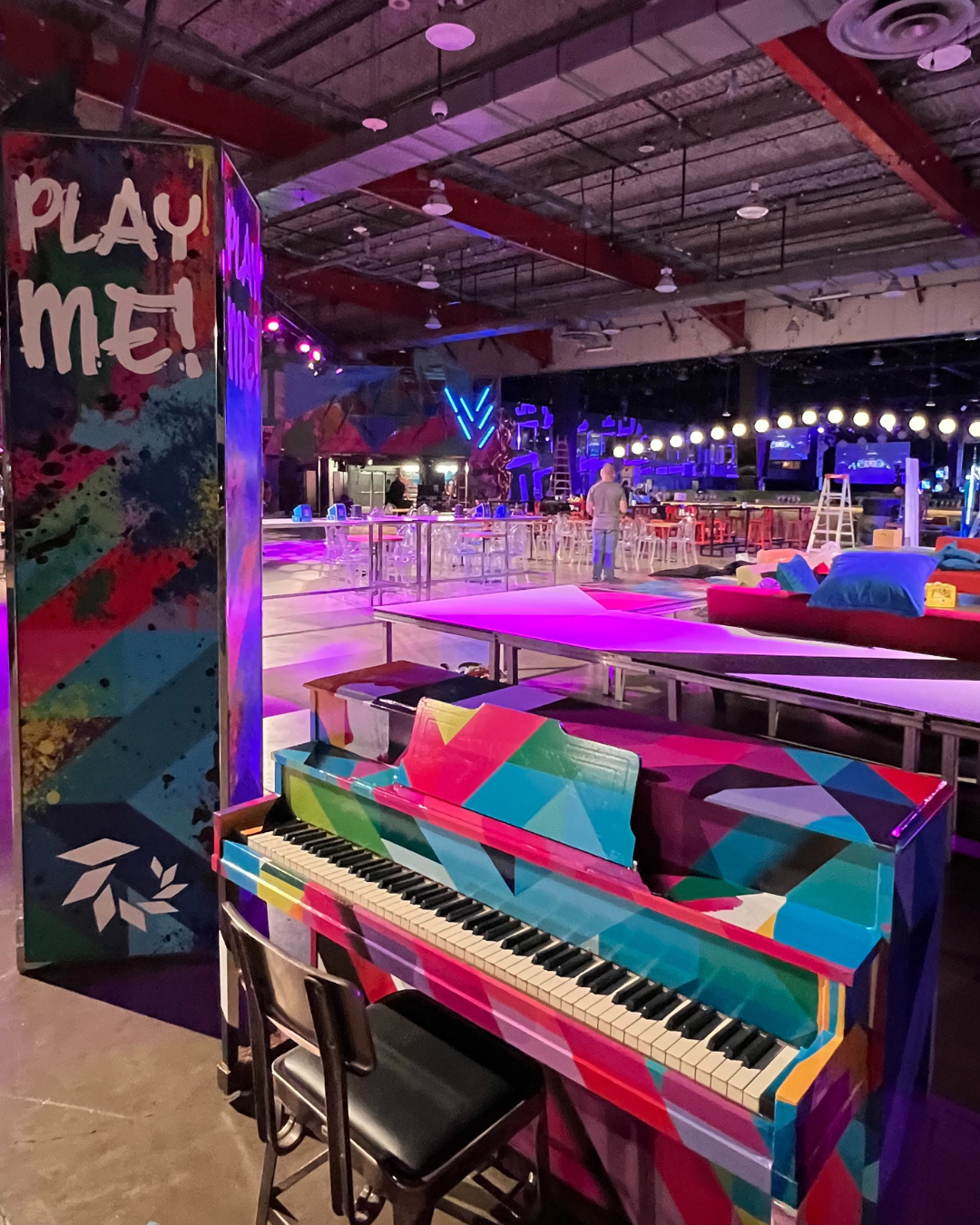 A colorful piano is sitting in front of a sign that says play me.