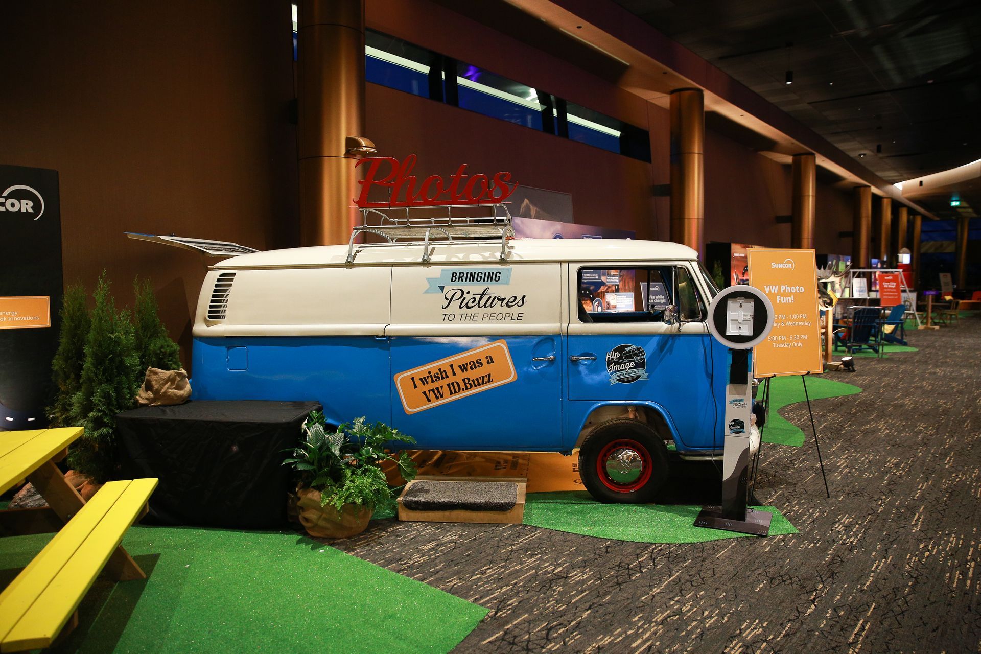 Blue and white vintage van with surfboards on top, set up as an event booth inside a building.