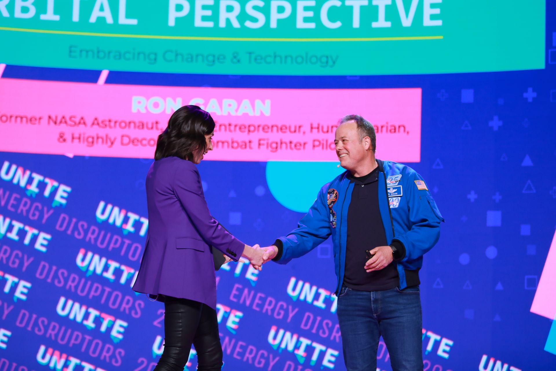 Two people shake hands on a stage. Text includes 