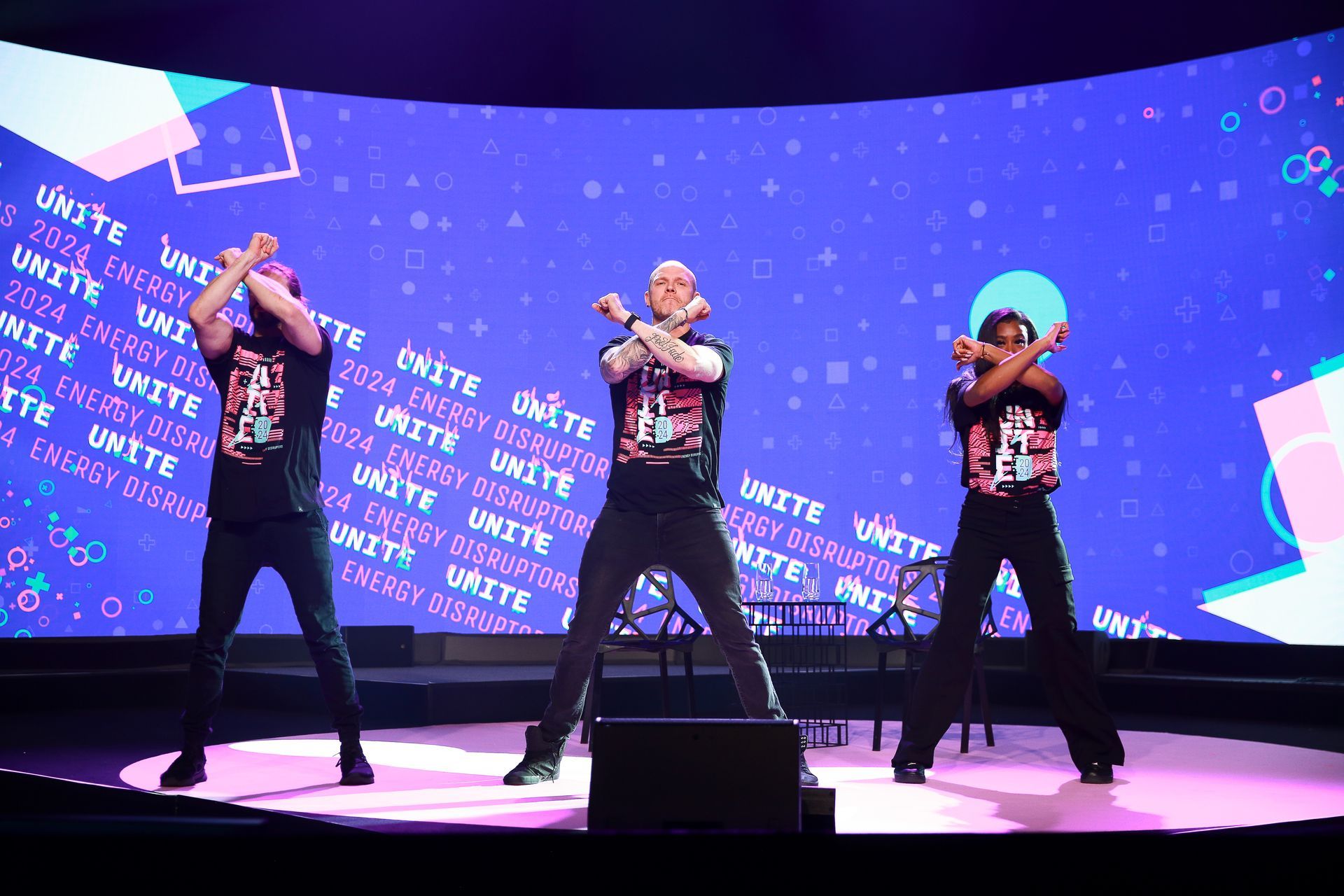Three people on stage, arms crossed, performing a dance. Backdrop with 