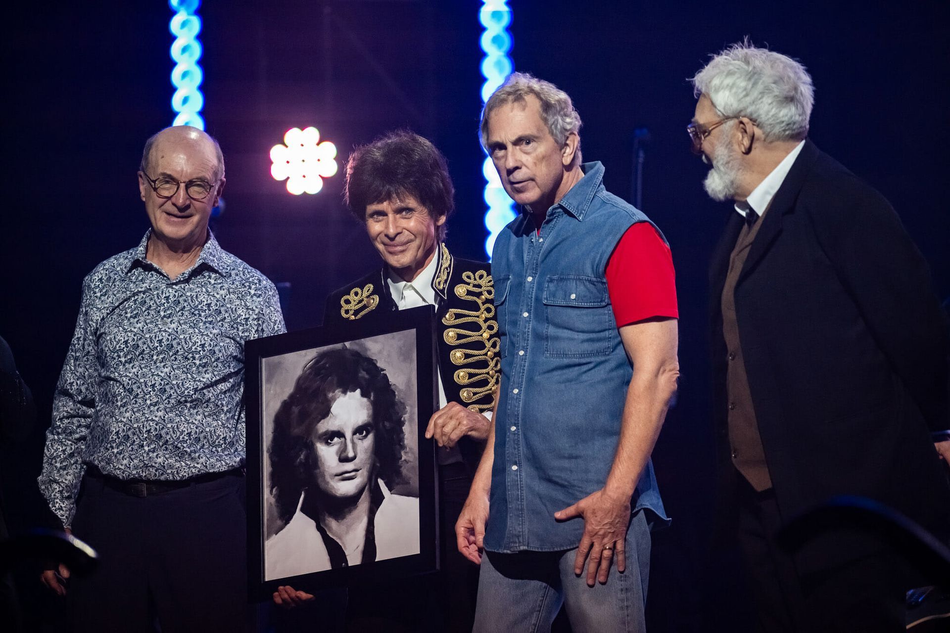 A group of men are standing next to each other on a stage holding a picture of a man.