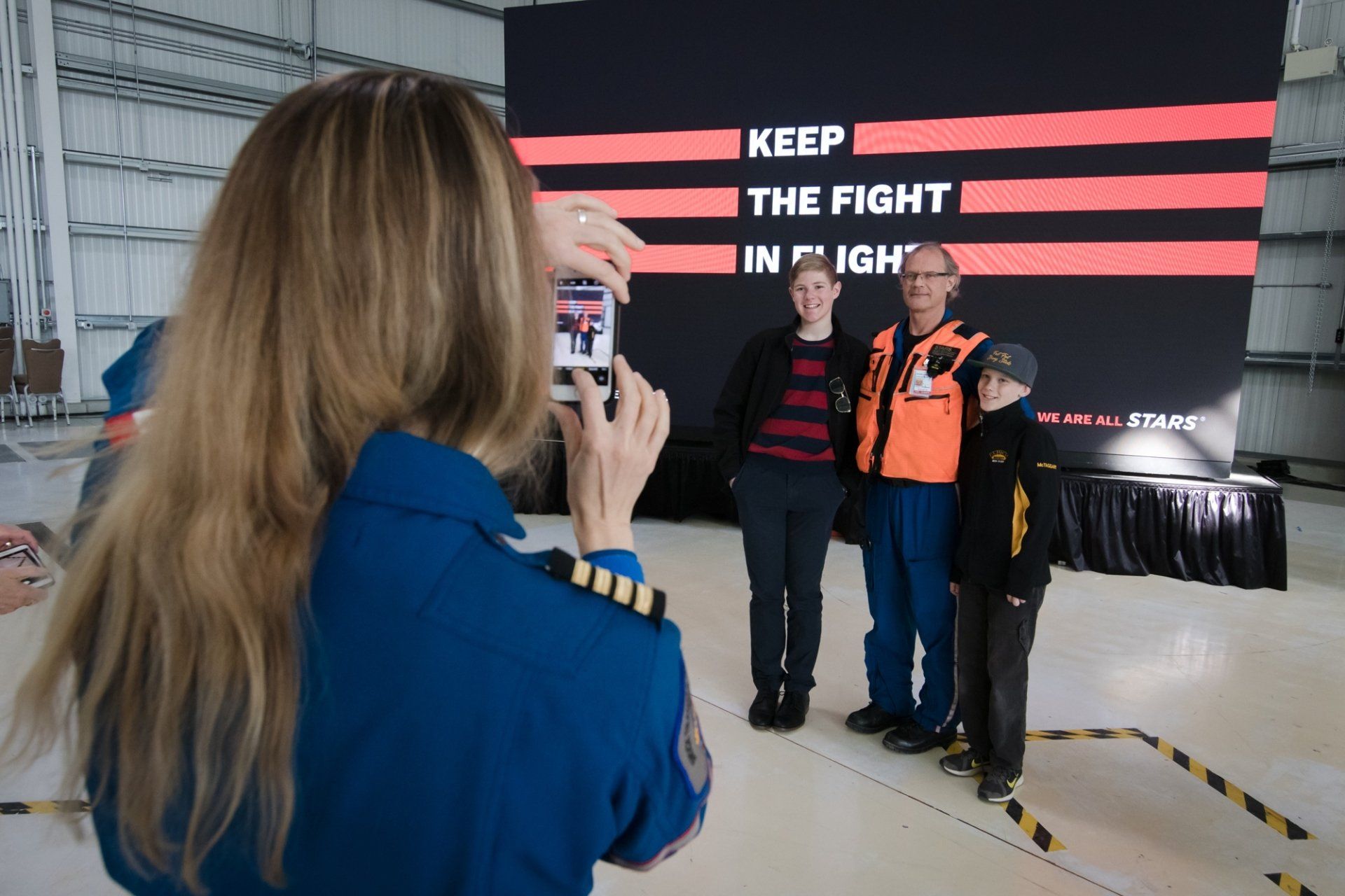 A woman is taking a picture of a group of people in a hanger.