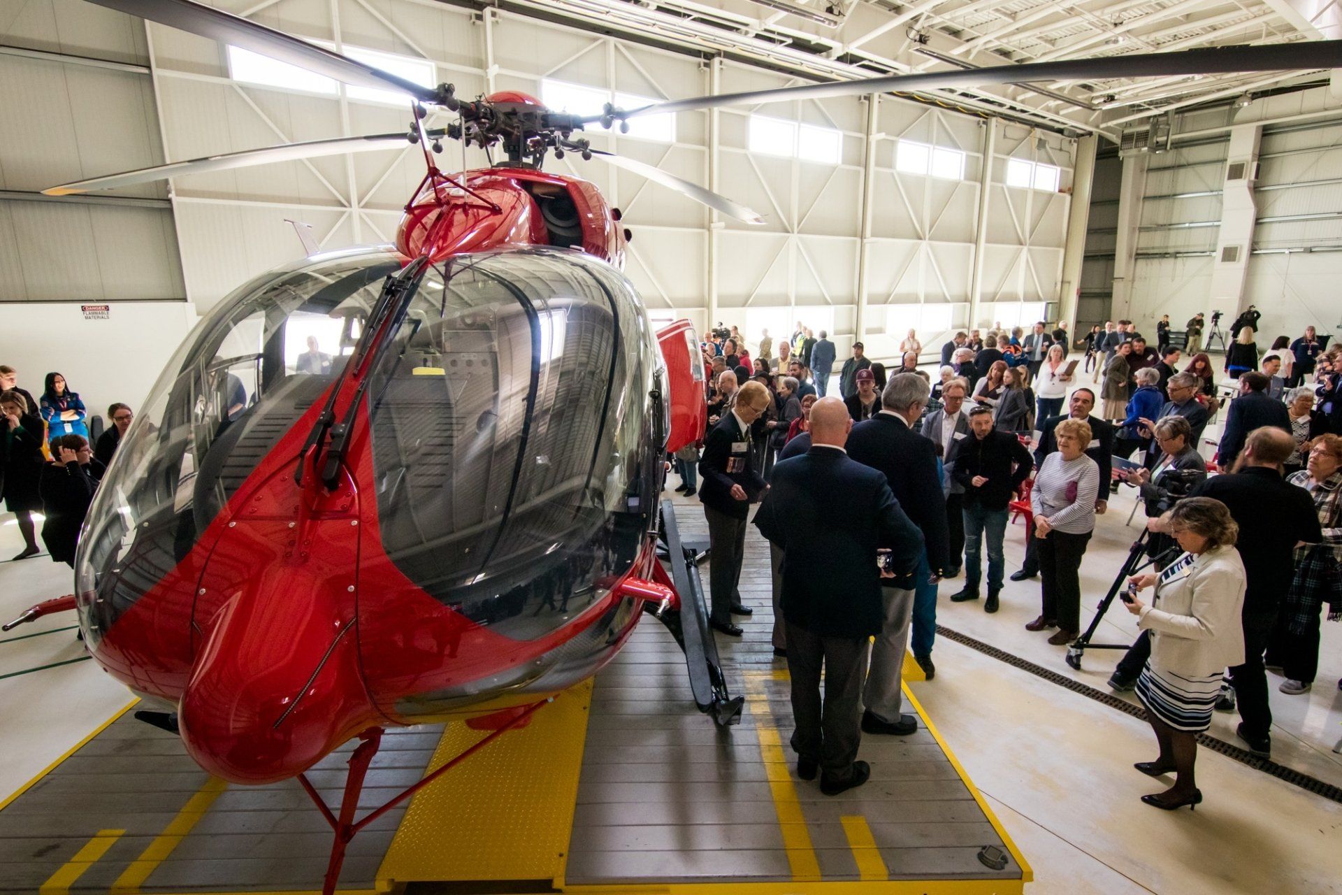 A group of people standing around a red helicopter in a hangar