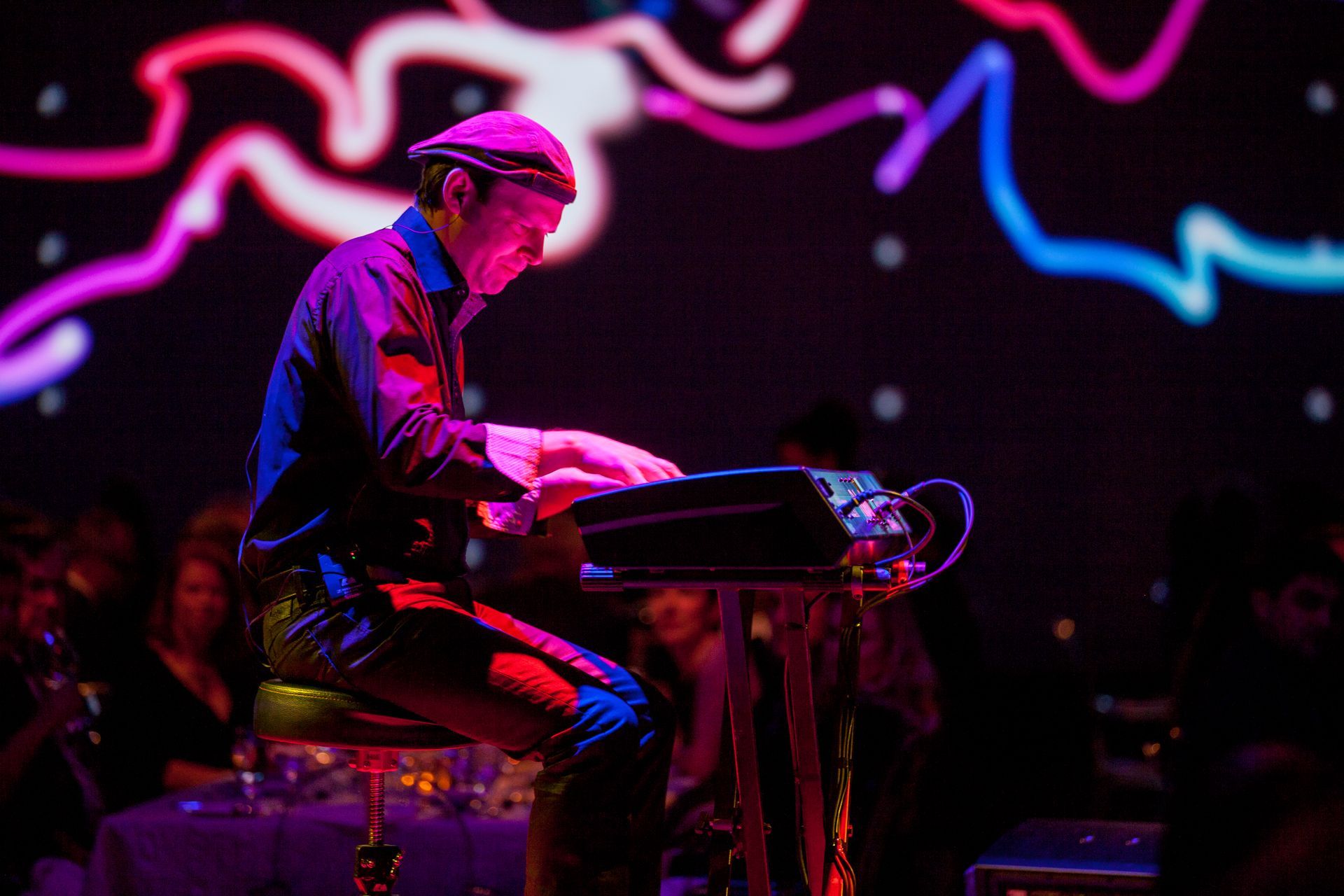 A man is sitting on a stool playing a keyboard on a stage.