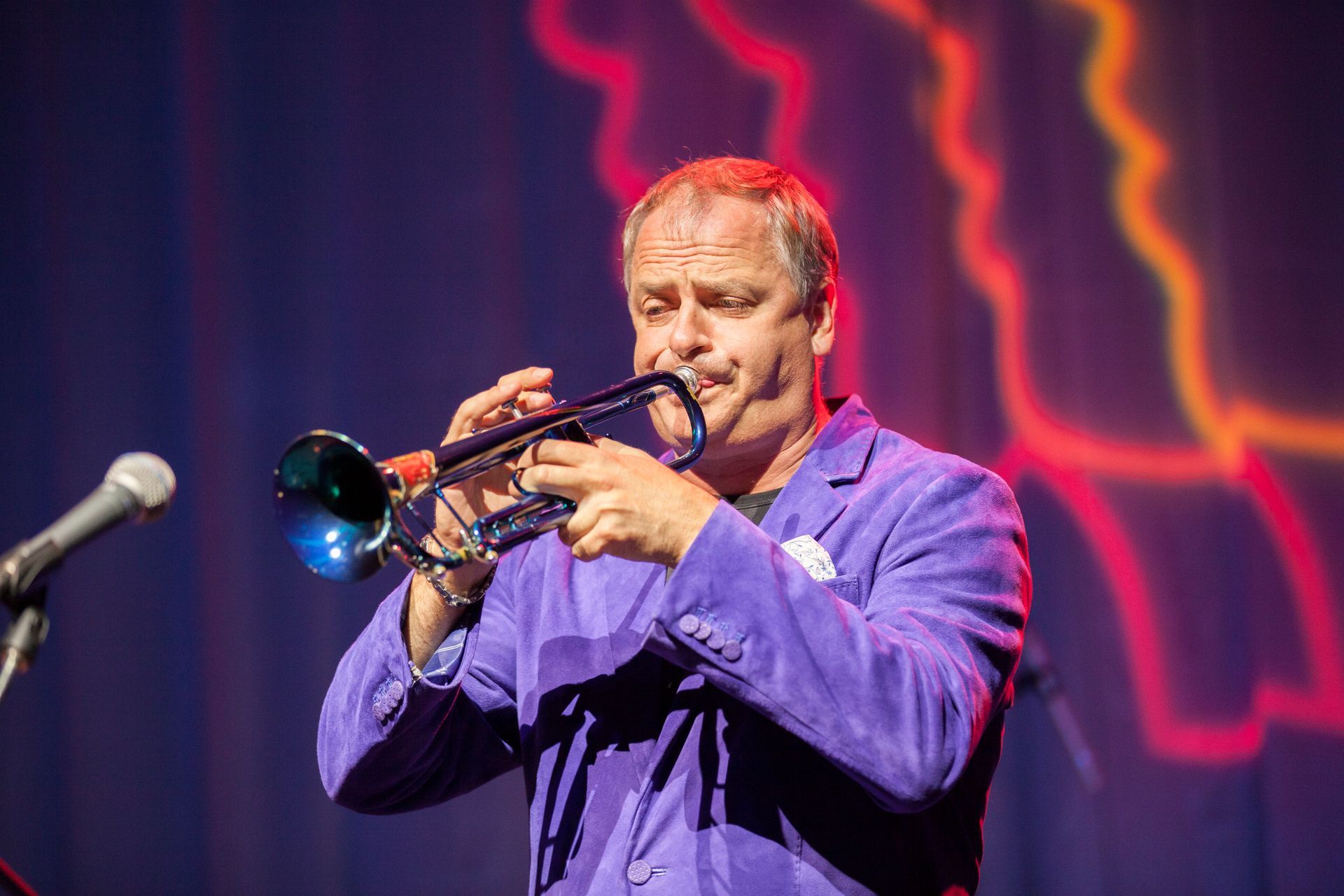 A man in a purple suit is playing a trumpet on a stage.