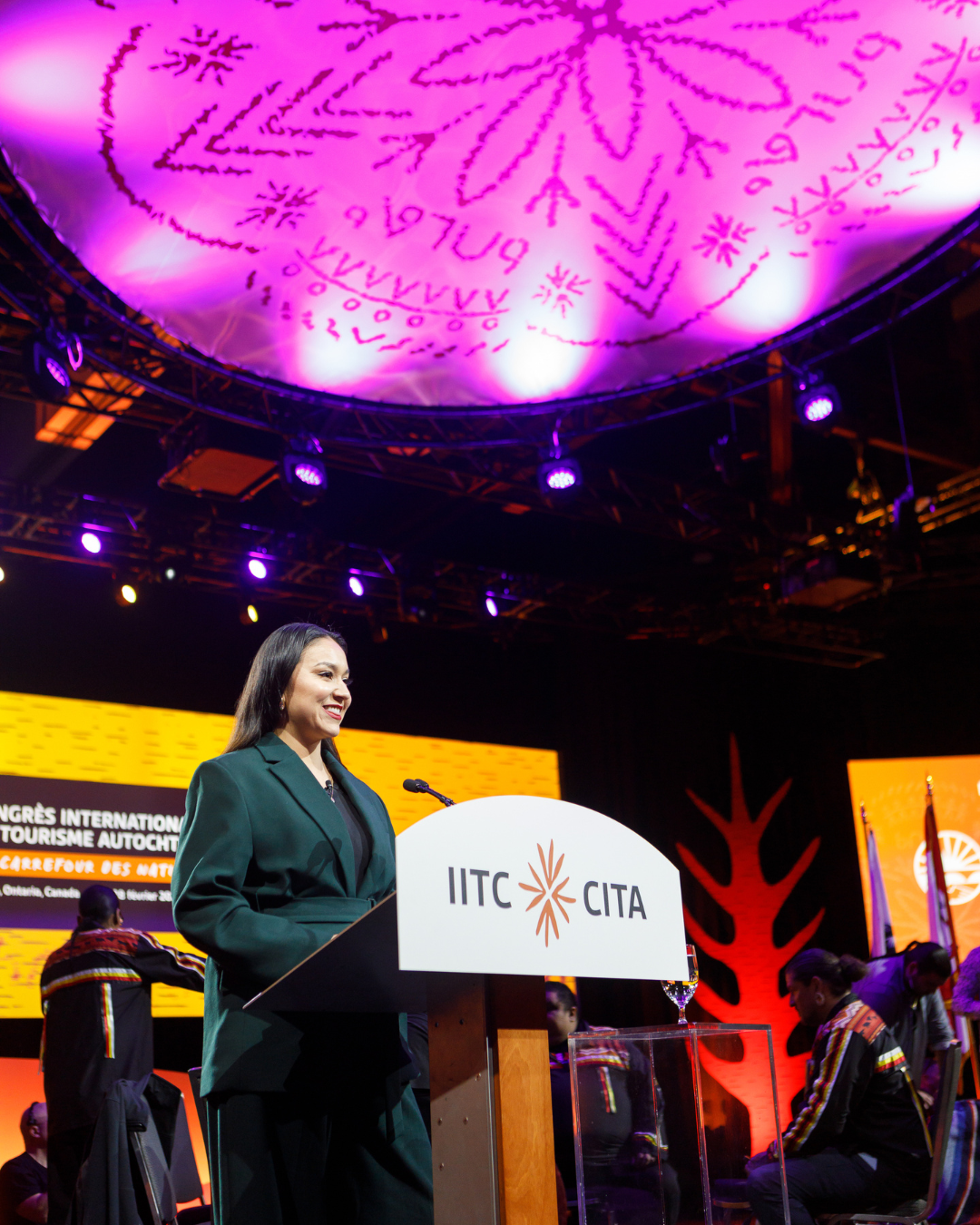 A woman stands behind a podium that says iitc cyta