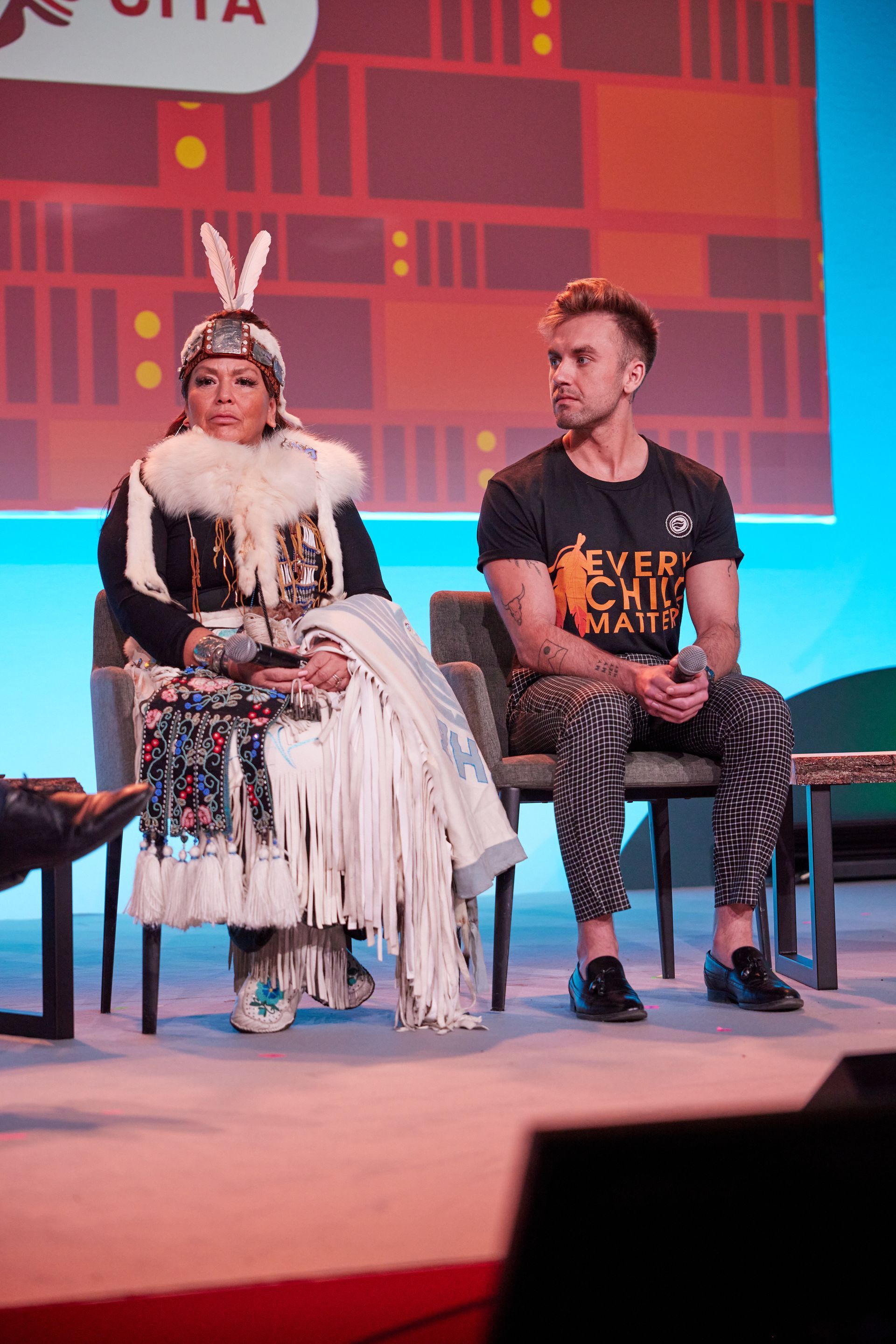 A man and a woman are sitting in chairs on a stage.