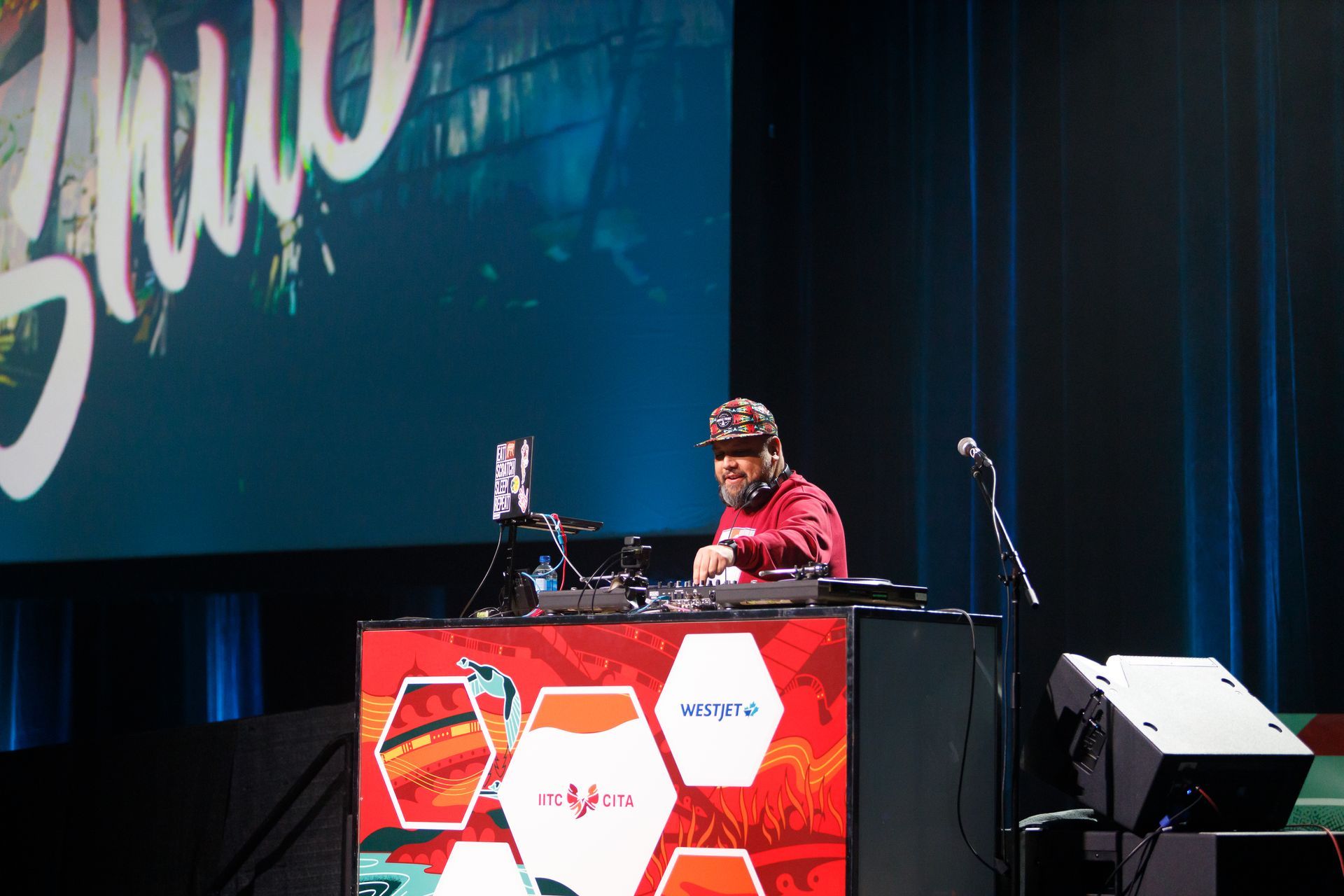 A man is playing a dj set on a stage with a large screen behind him that says ' zulu '