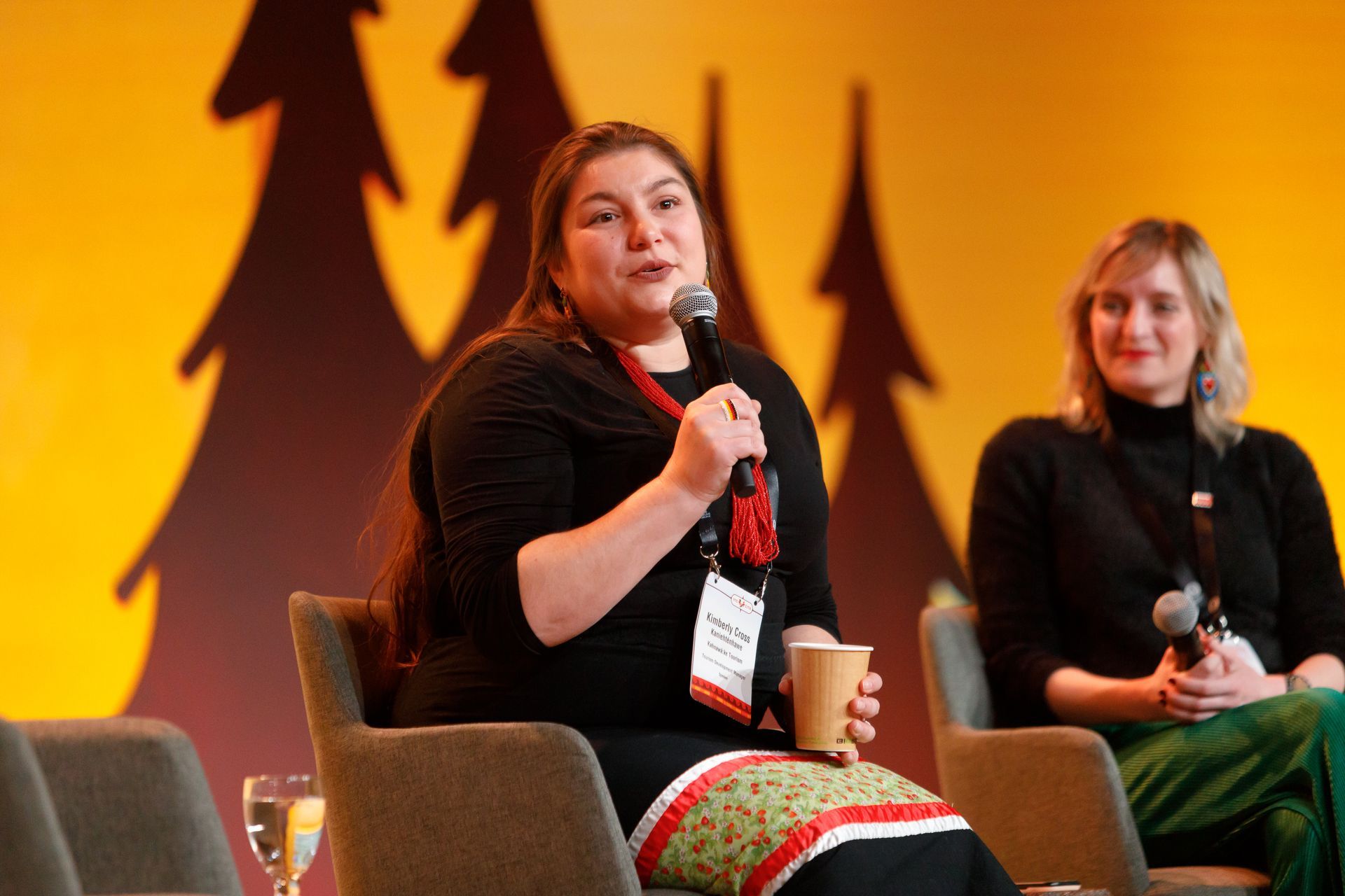 A woman is sitting in a chair holding a microphone and a cup of coffee.