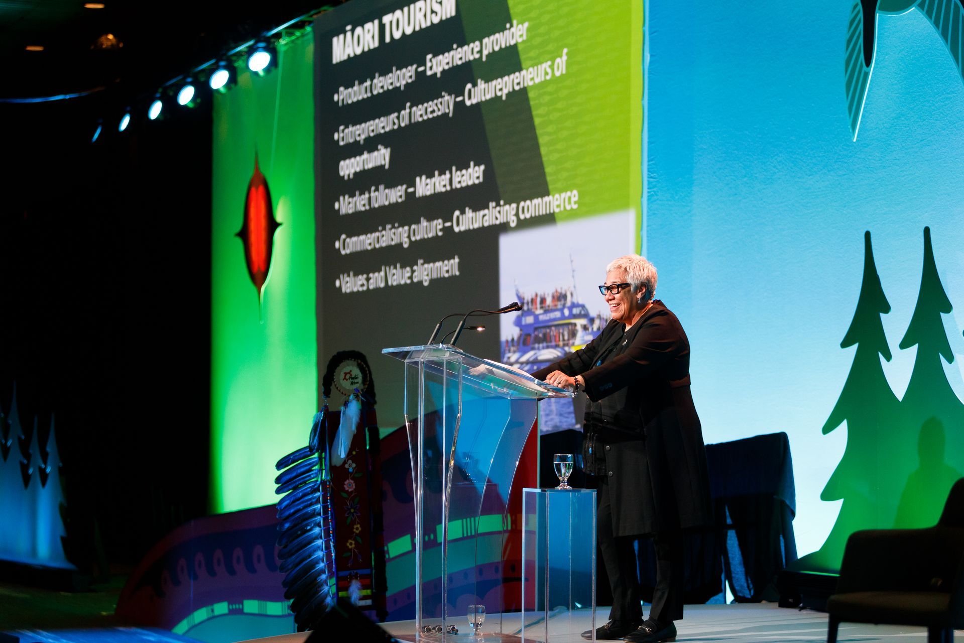 A man is standing at a podium giving a speech in front of a large screen.
