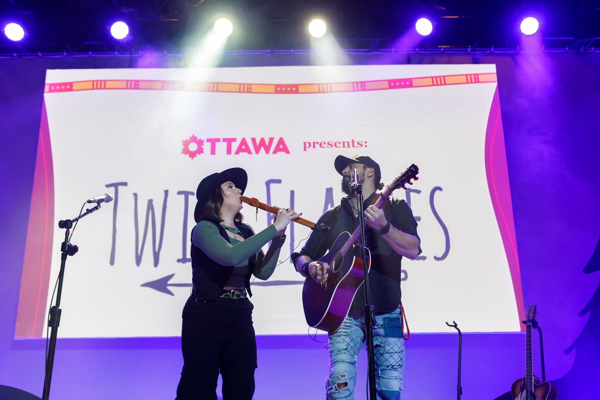A man and a woman are playing guitars on a stage.
