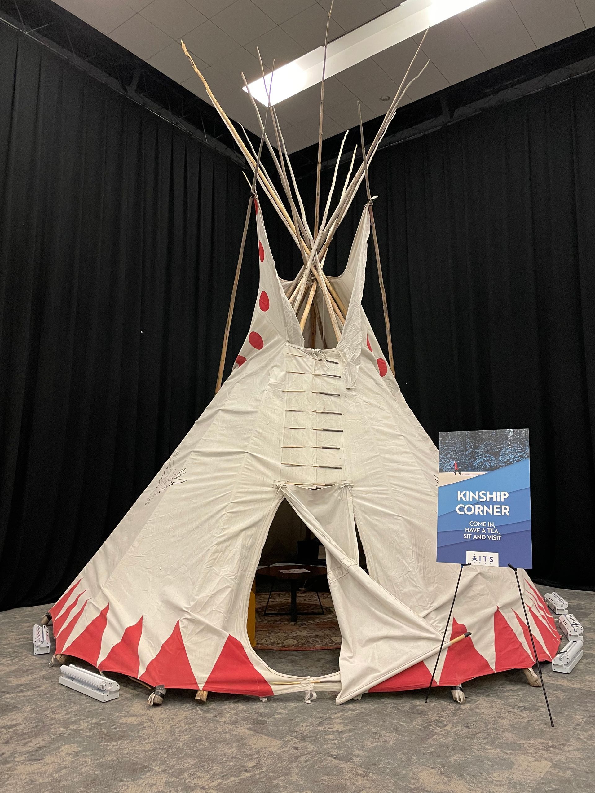 A teepee is sitting in front of a black curtain in a room.