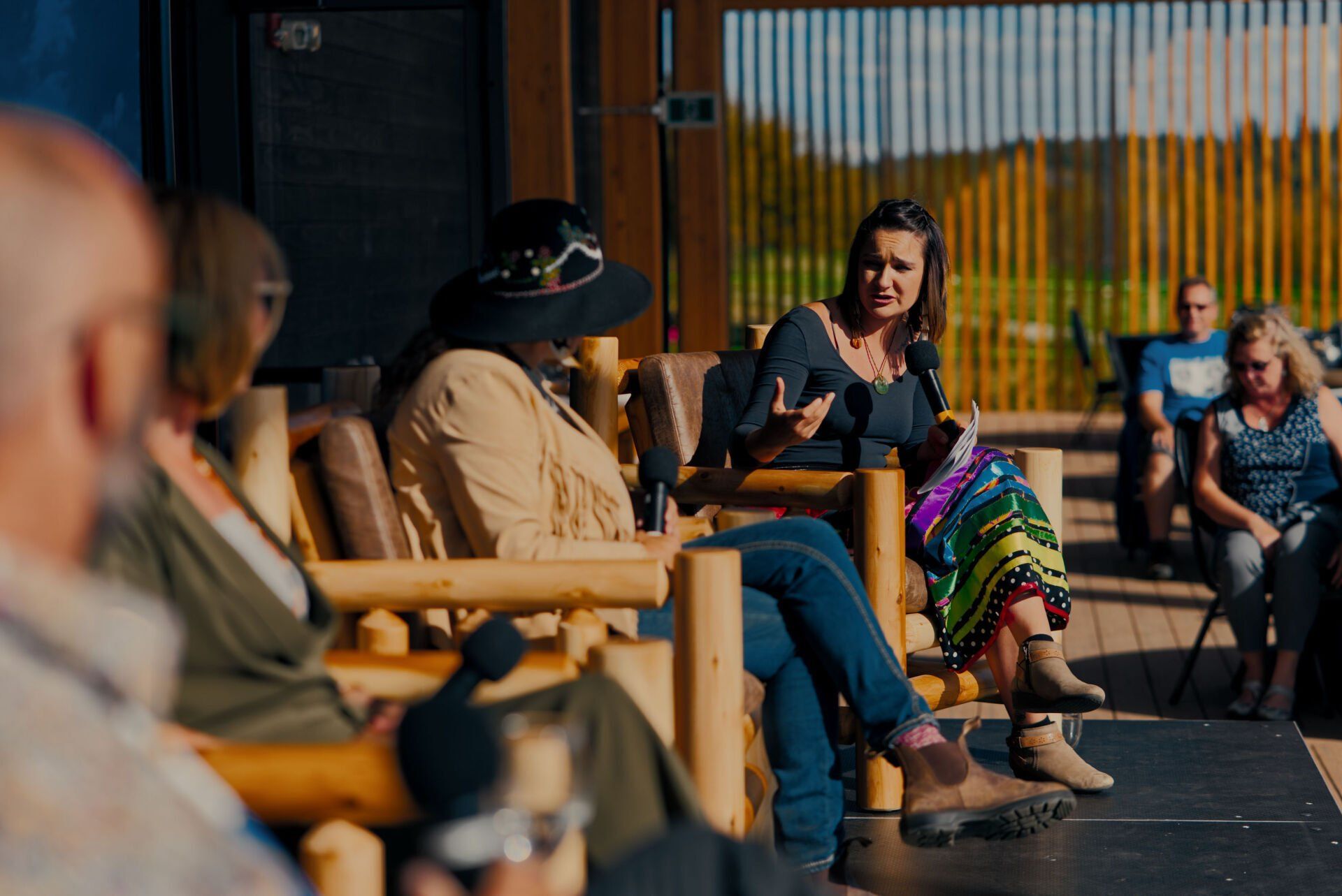 A group of people are sitting in wooden chairs talking to each other.