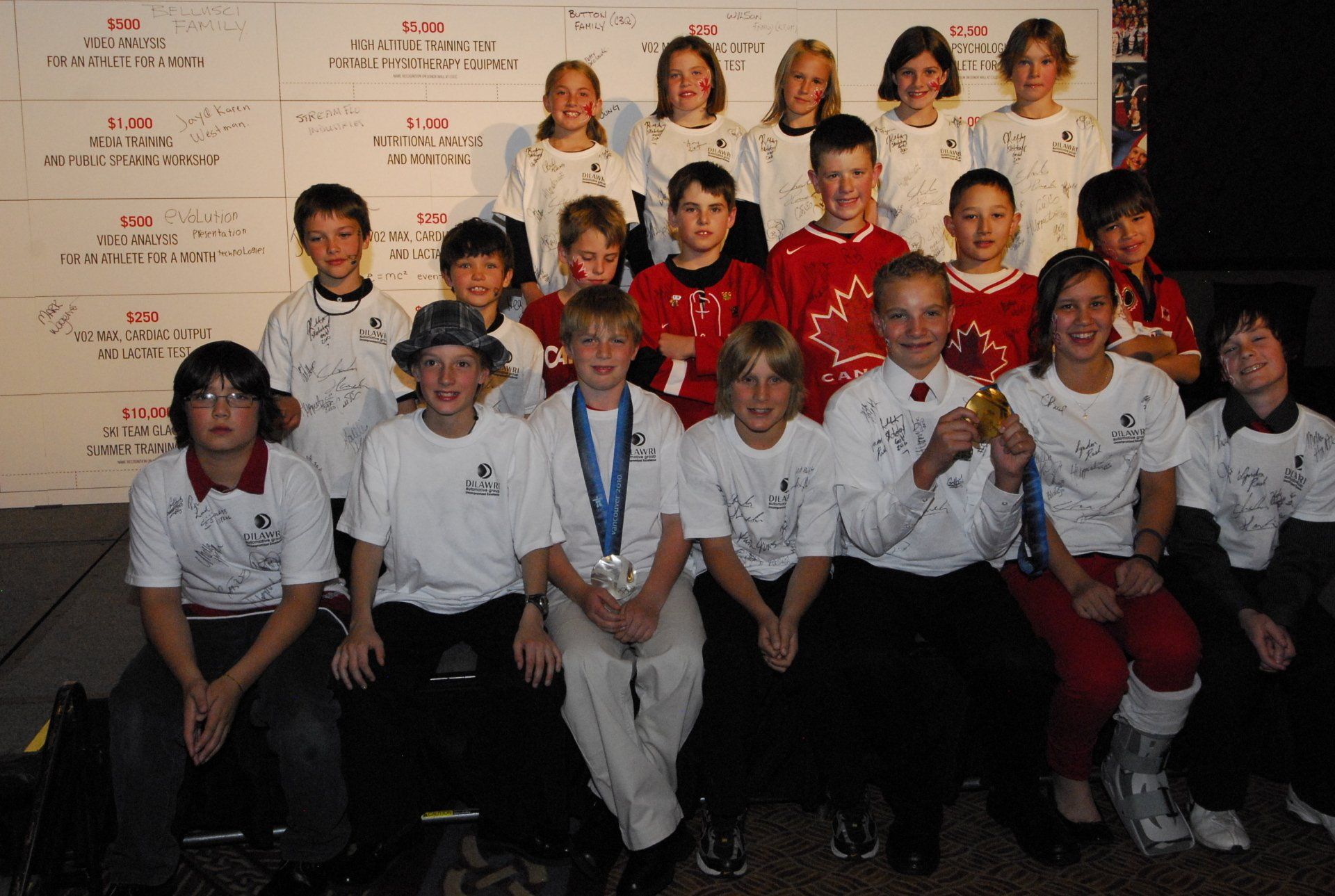 Group of children in matching shirts posing with a backdrop; some hold medals.