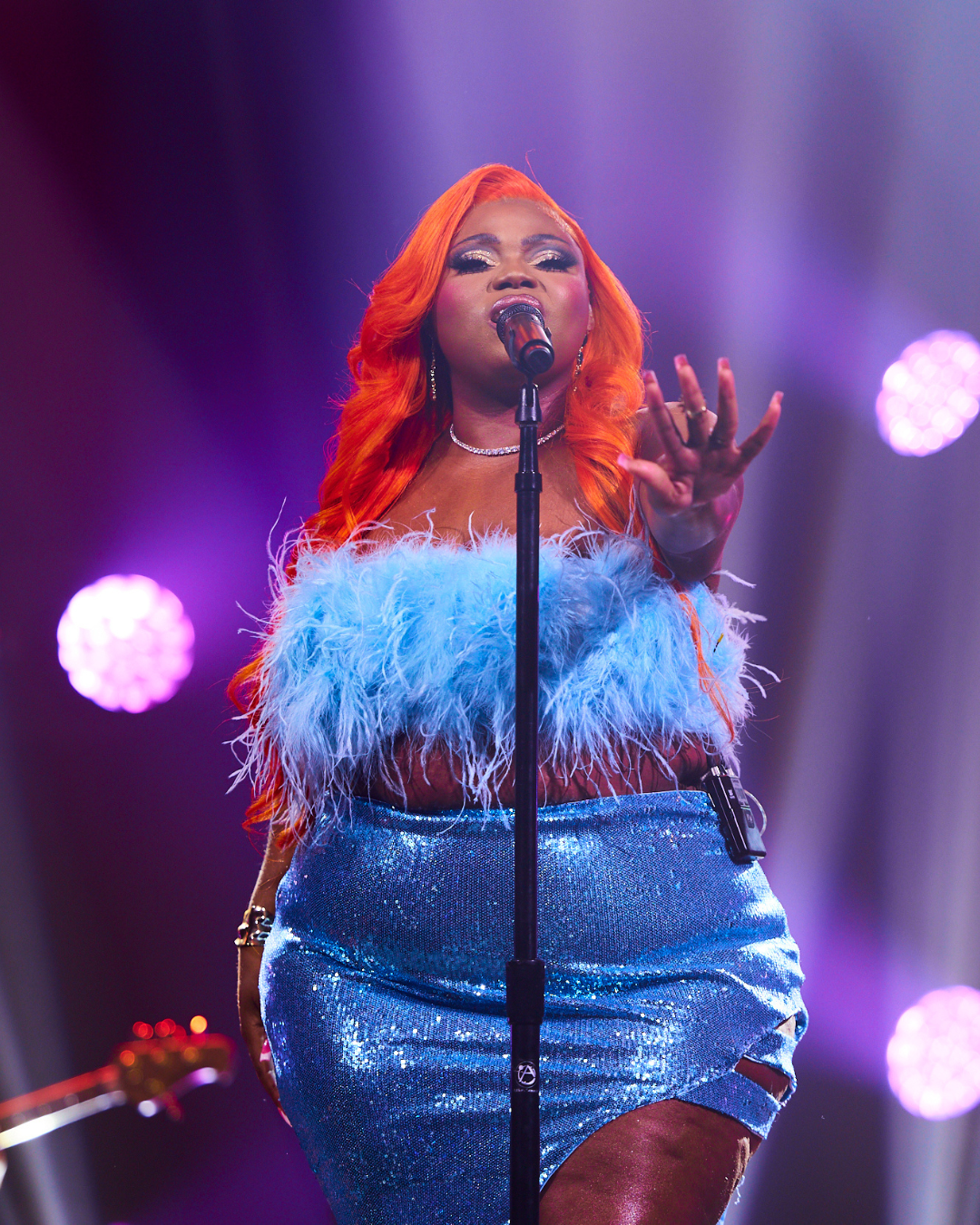 A woman with red hair is singing into a microphone on a stage.