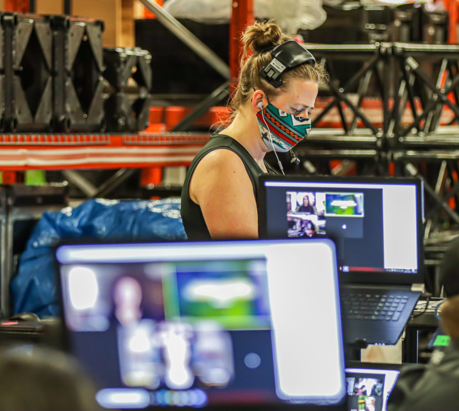 A woman wearing a mask is sitting in front of a computer screen.
