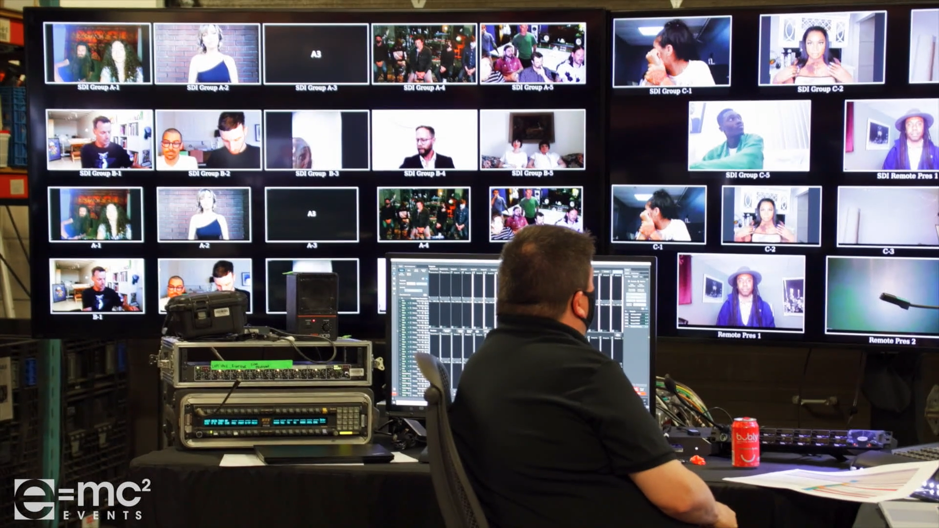 A man sits at a desk in front of a wall of monitors that says e = mc