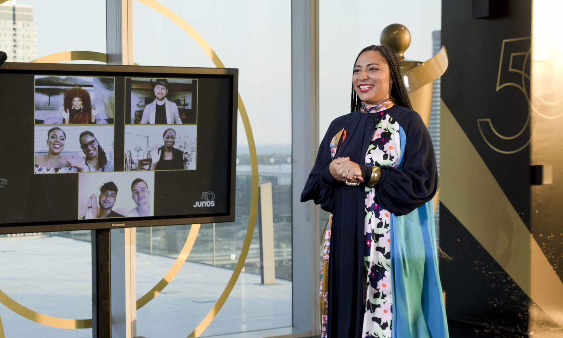 A woman is standing in front of a large screen with a group of people on it.
