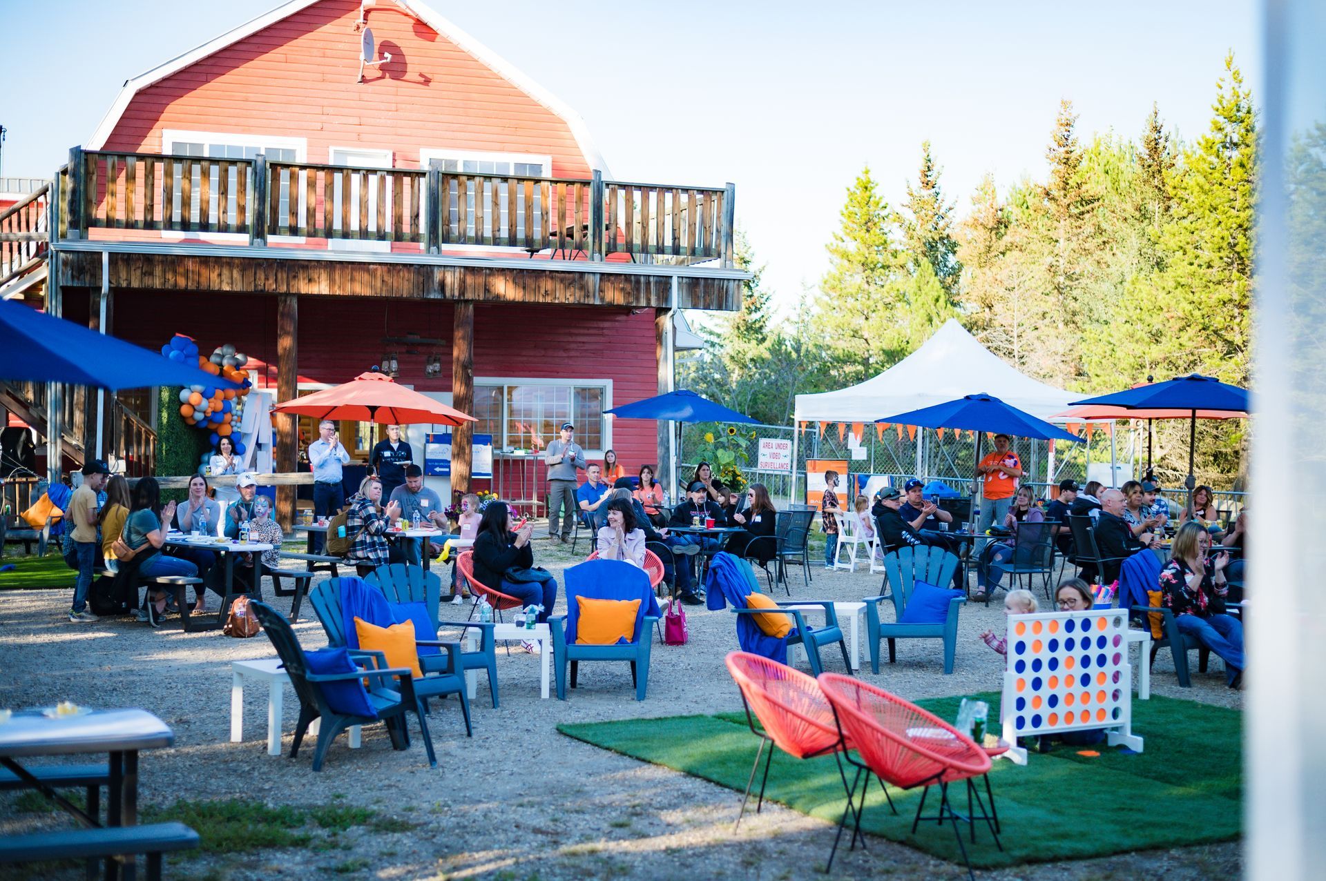 A group of people are sitting at tables and chairs in front of a red barn.