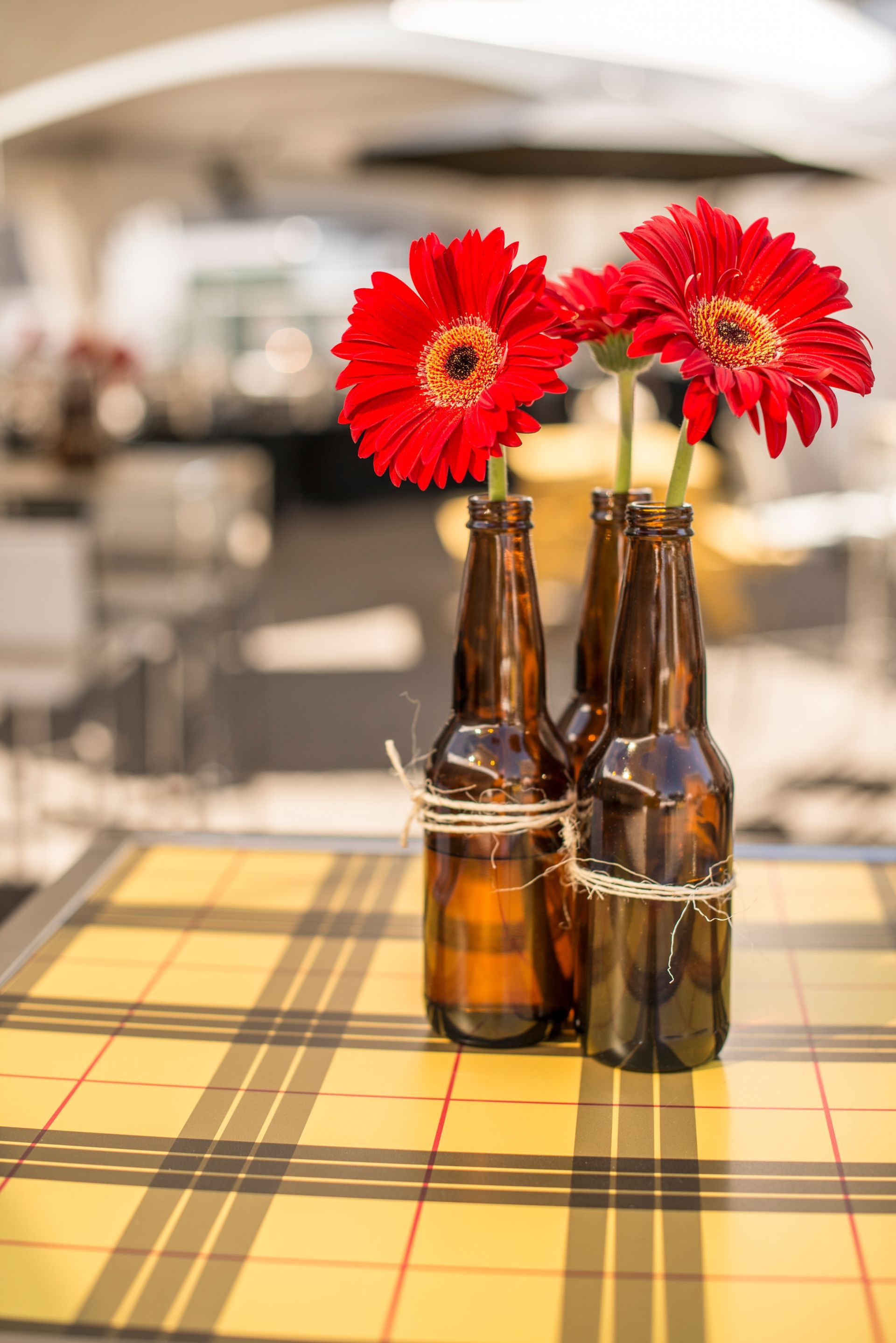 Three brown bottles filled with red flowers are sitting on a table.