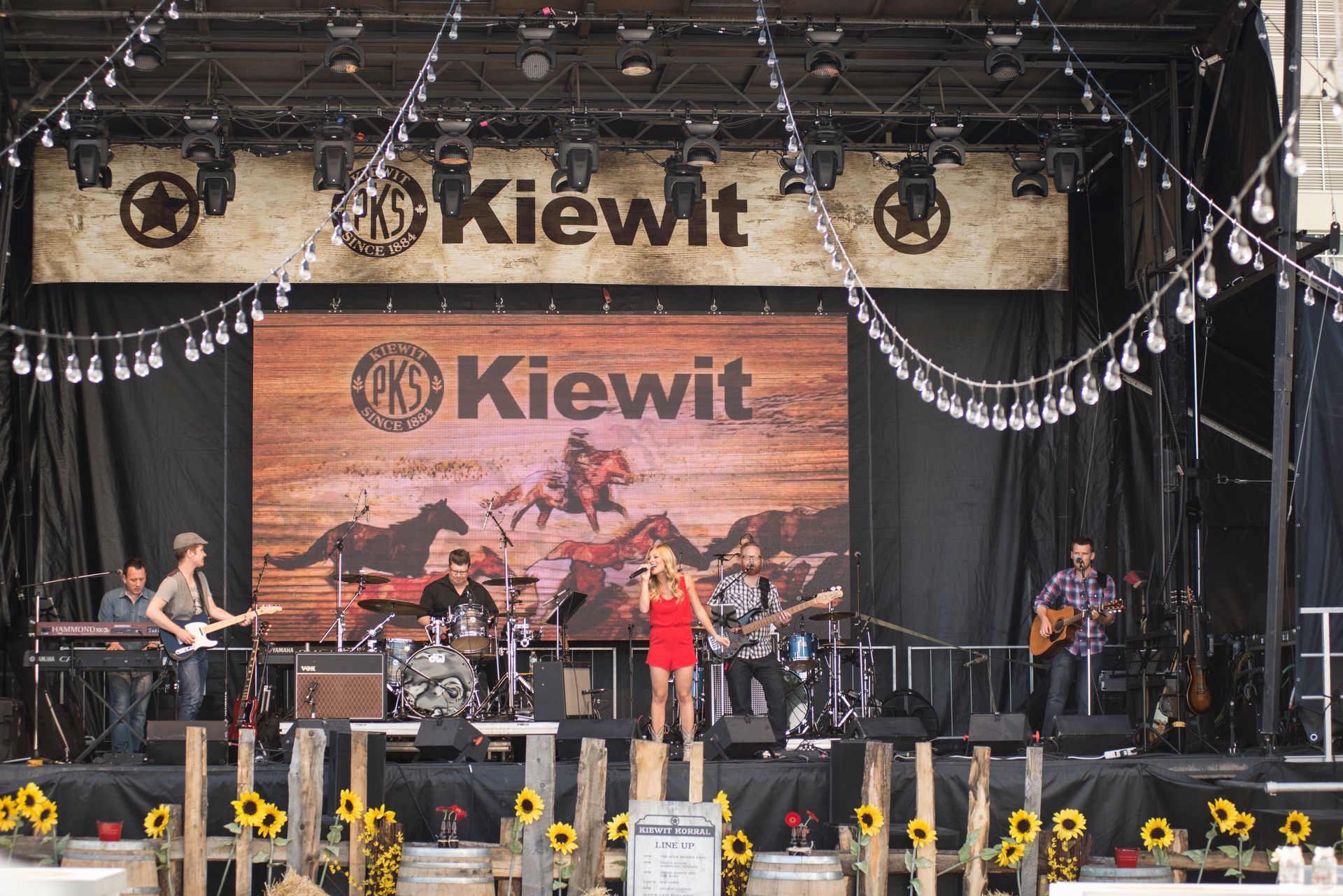 A woman singing on a stage in front of a sign that says kiewit