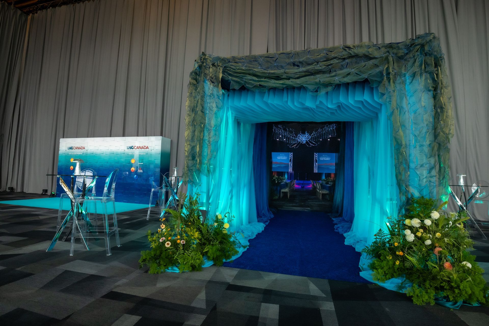 An underwater-themed entrance with blue curtains, floral arrangements, and a dark blue carpet leading to a stage.