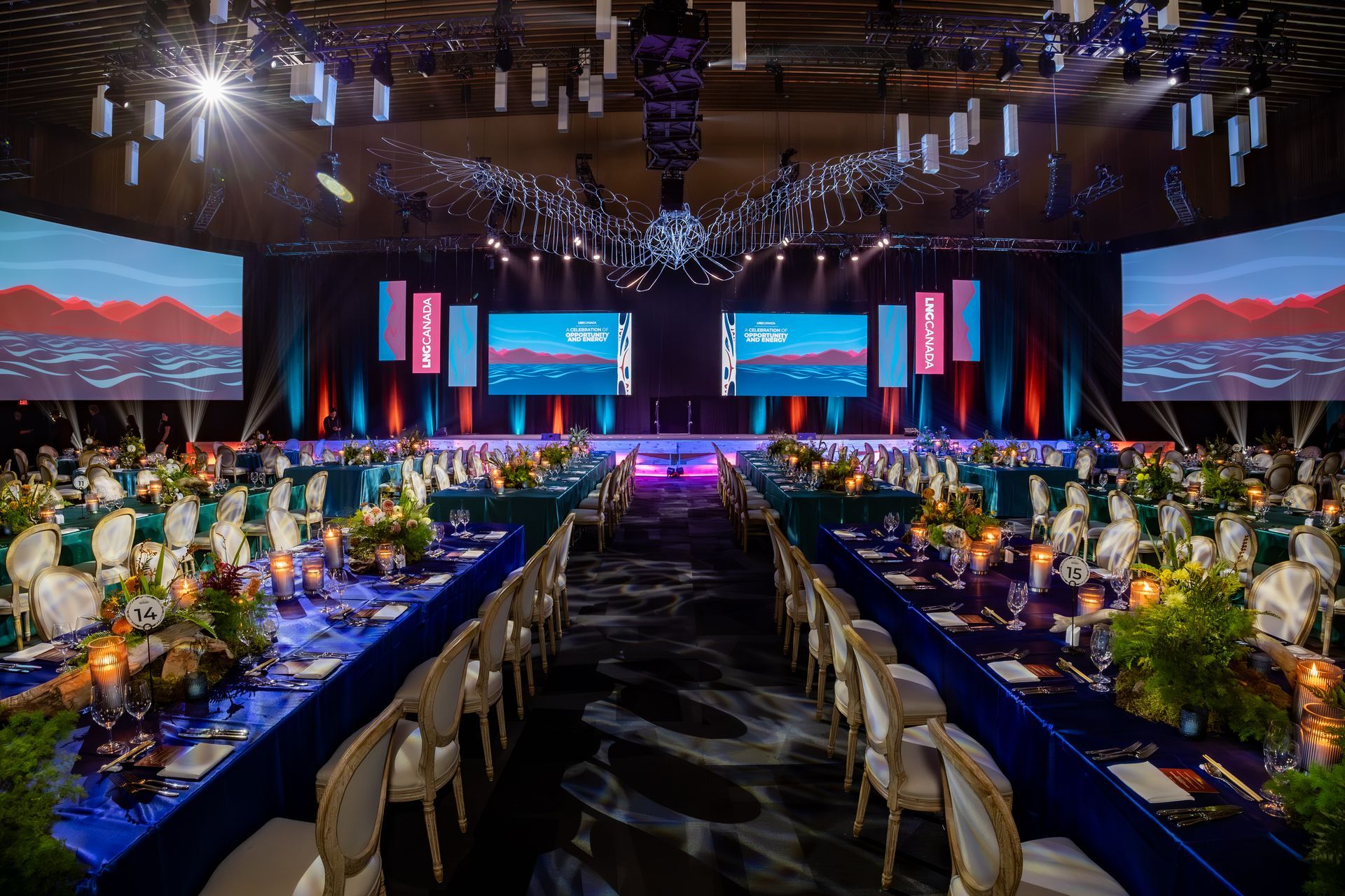 Elegant banquet hall with long tables set for dinner, stage with screens. Blue and white decor.