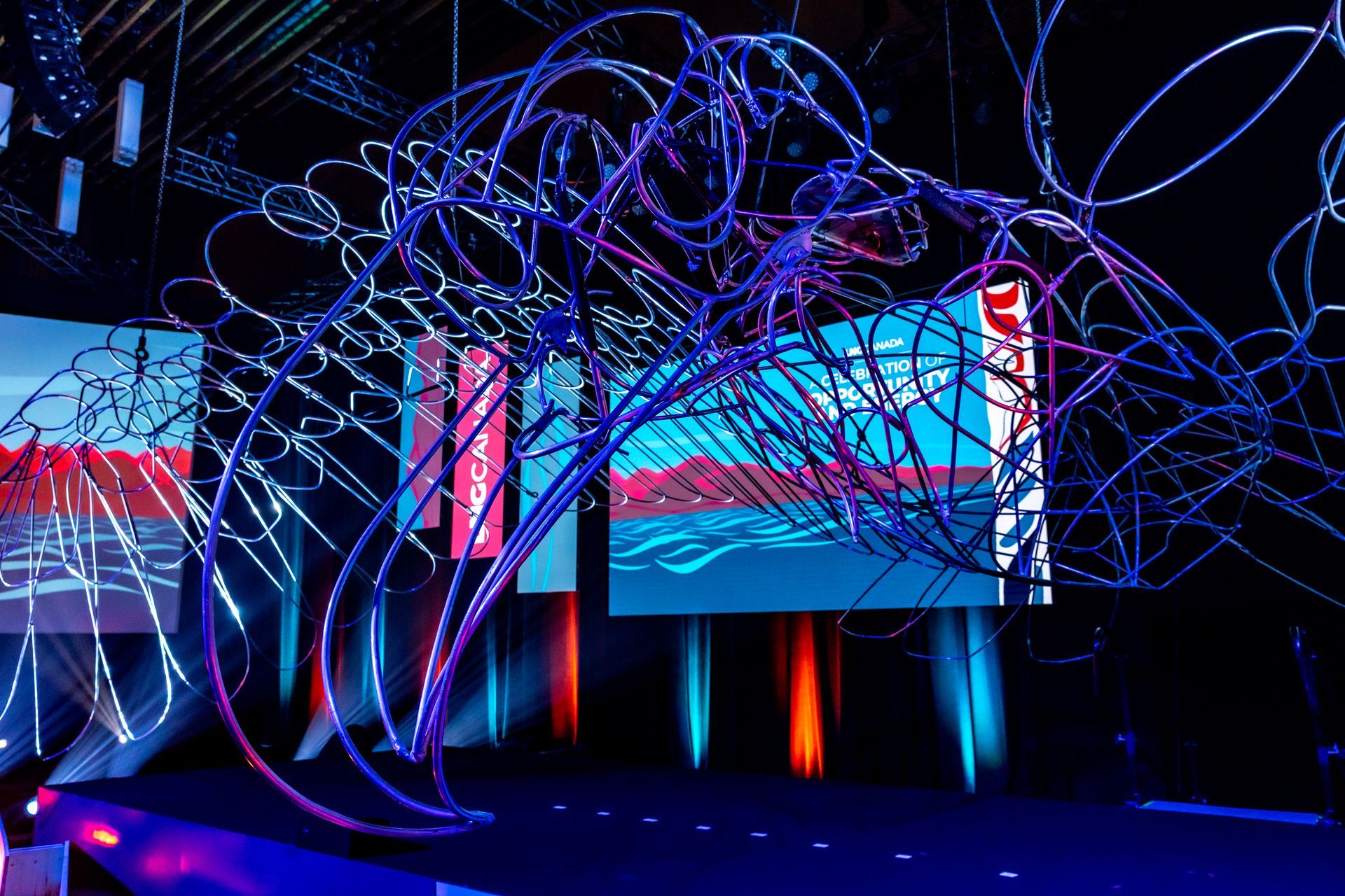 Abstract art installation with glowing blue and purple lines in front of screens displaying landscapes.