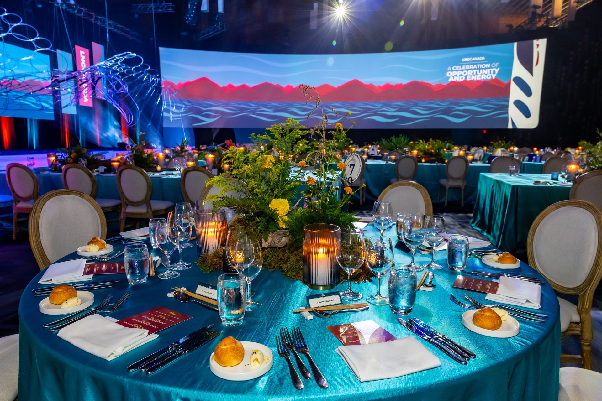 Elegant round table set for a formal event with teal tablecloth, centerpieces, and place settings.