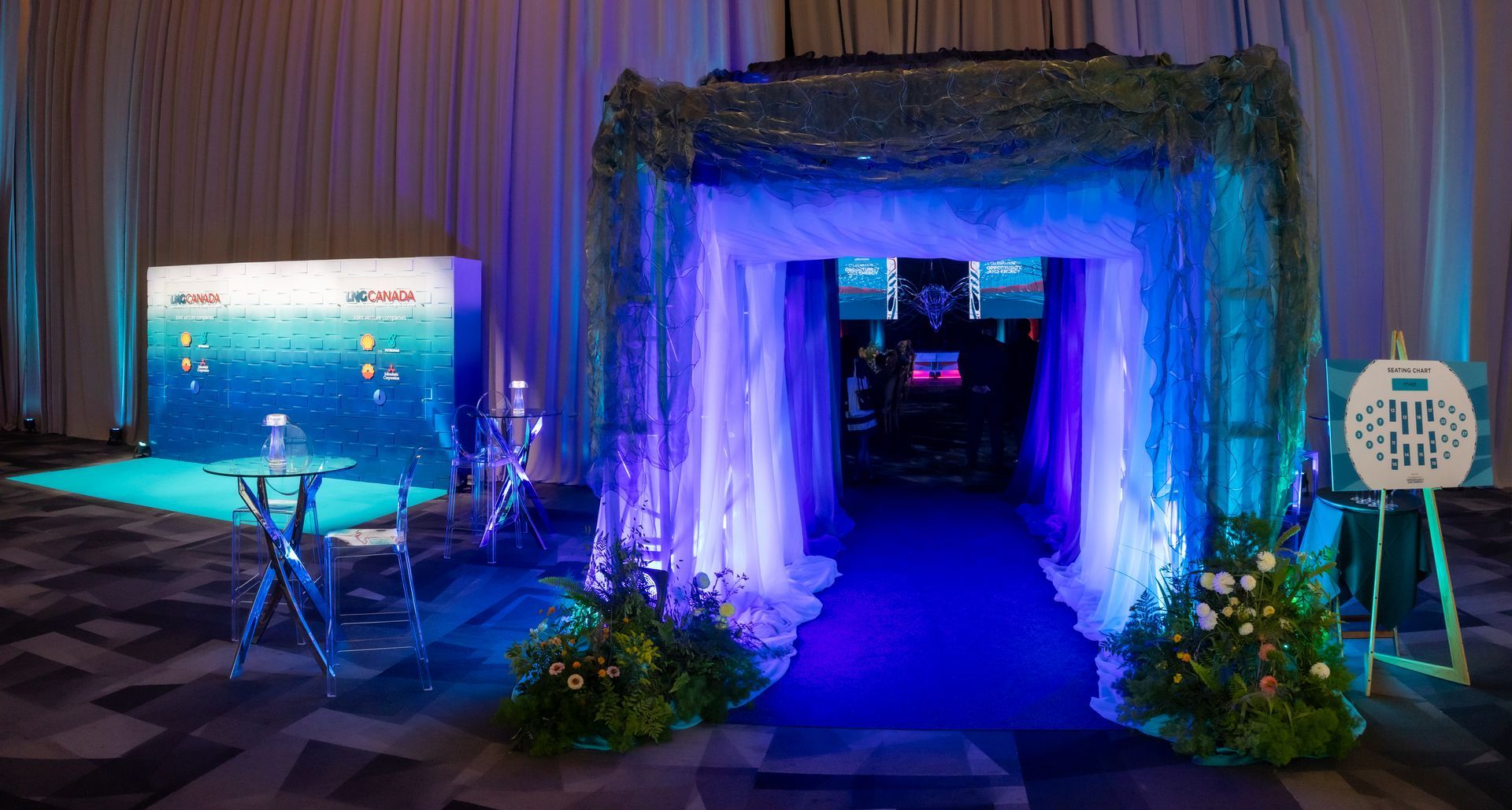 Entrance to an event with blue lighting, draped fabric, and floral decorations.