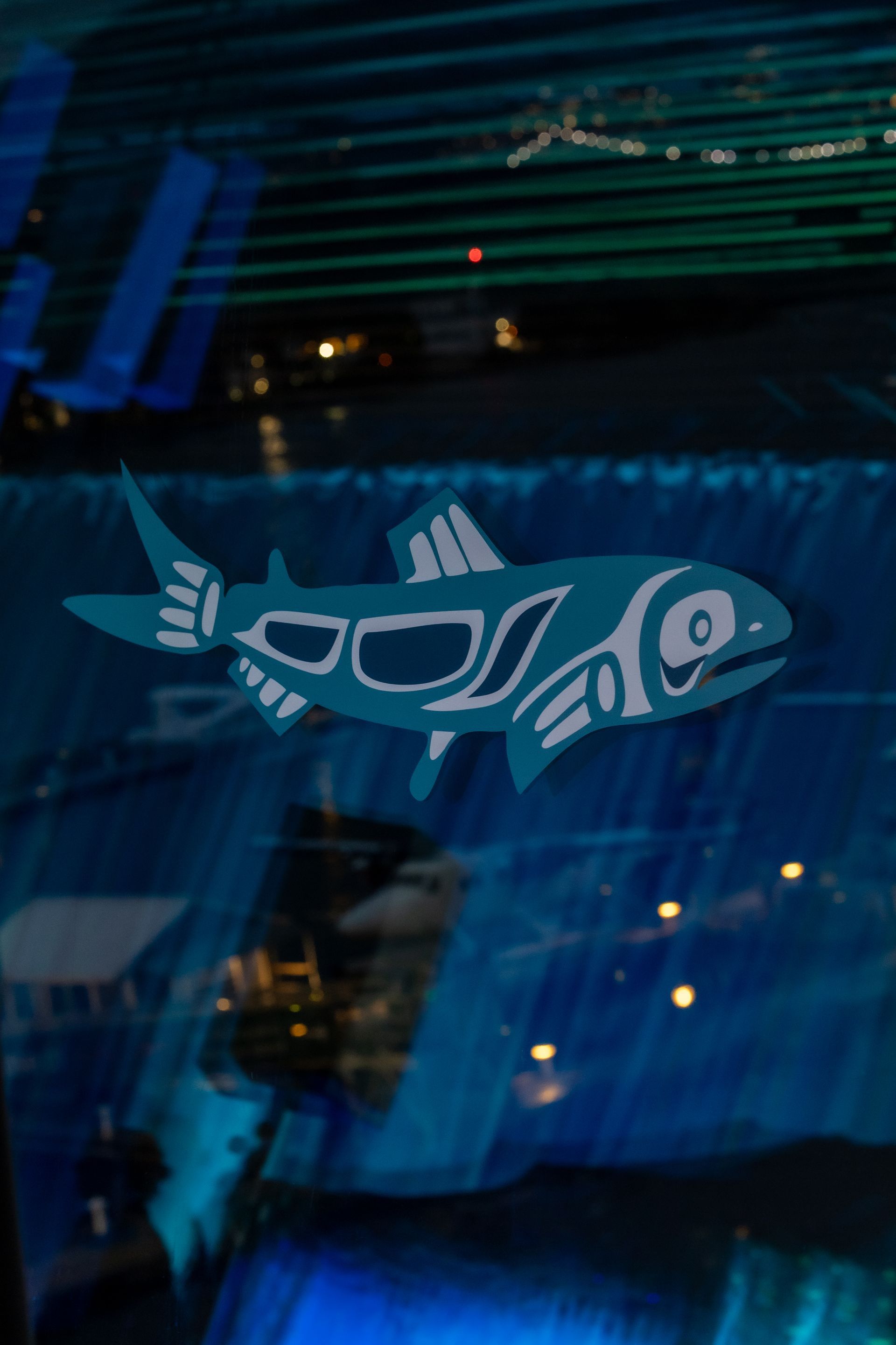 Teal Native American-style fish graphic against blue and green abstract background.