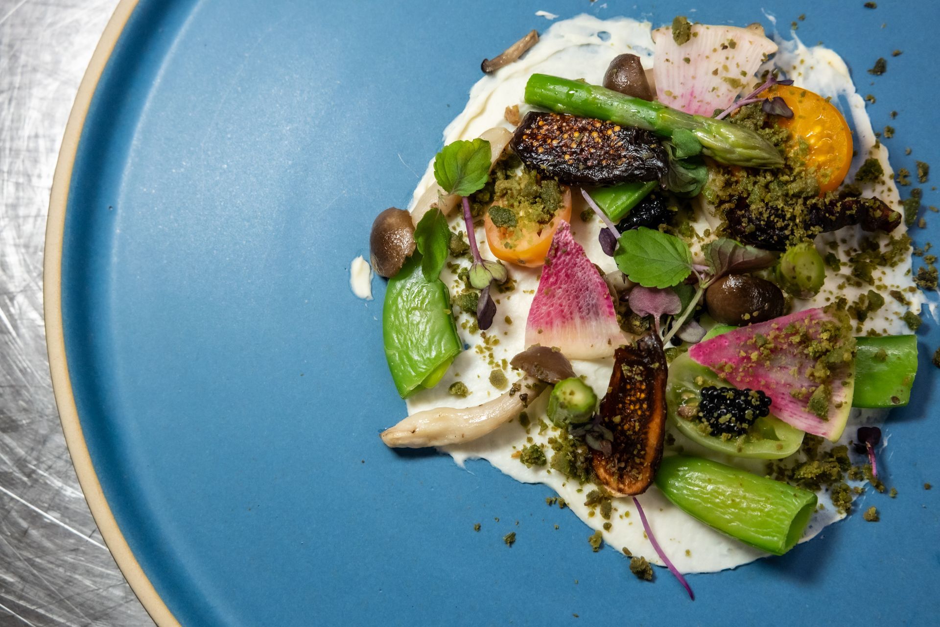 A colorful gourmet dish on a blue plate, featuring vegetables and a creamy sauce.