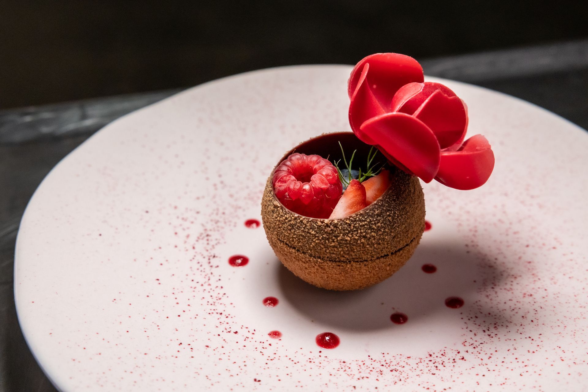 Chocolate dessert with raspberries, strawberries, and a decorative rose on a white plate.