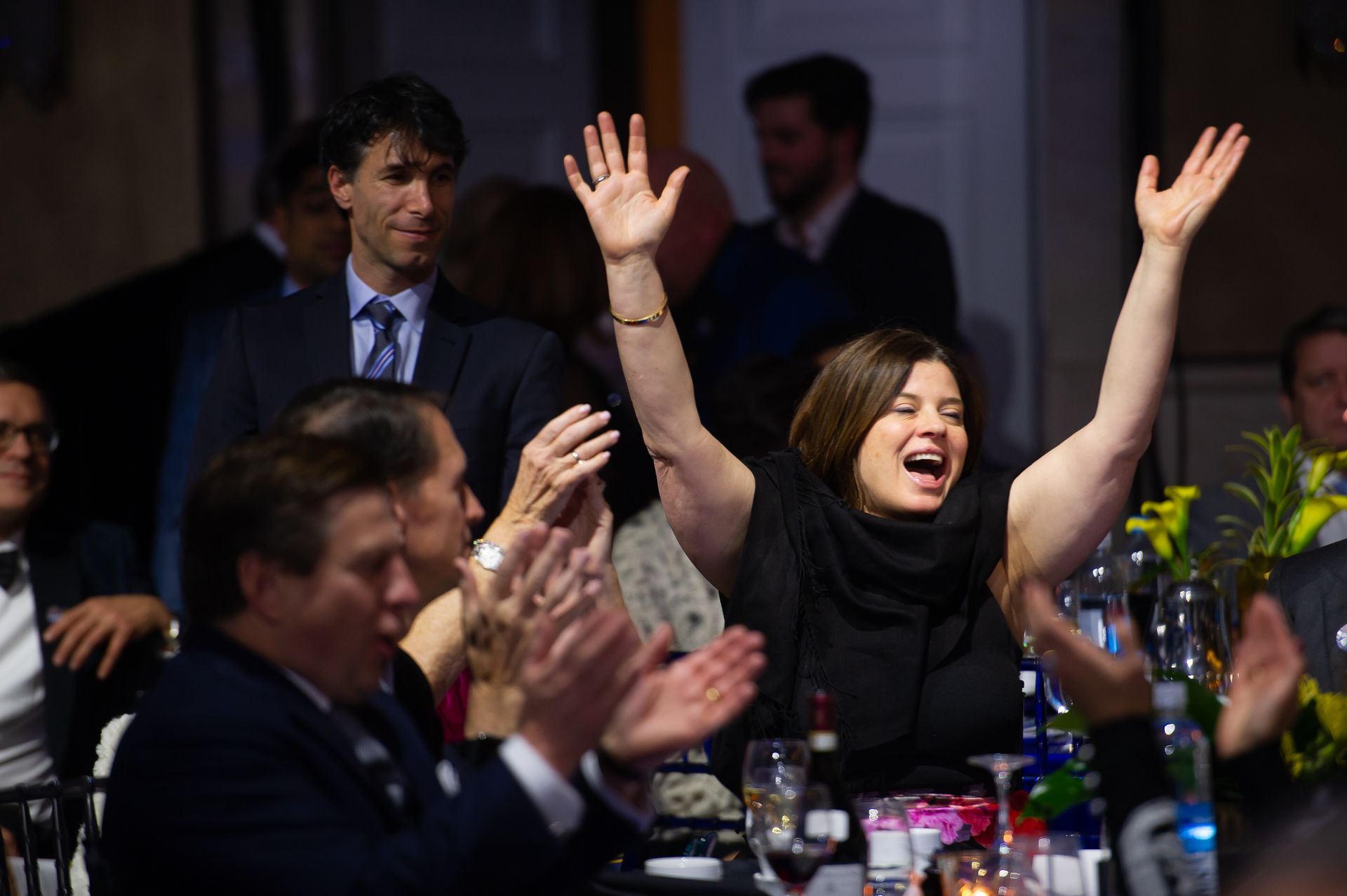 A woman is sitting at a table with her hands in the air.