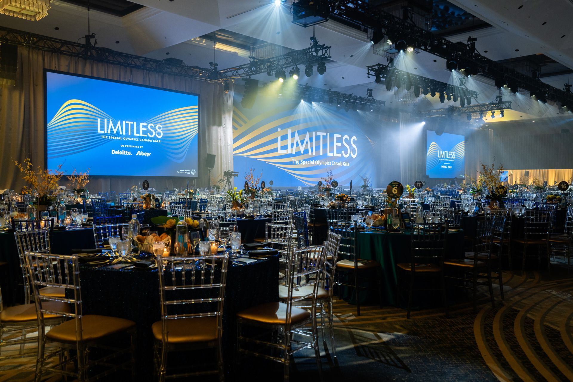 A large ballroom filled with tables and chairs and a large screen.