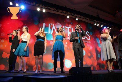 A group of people singing on a stage with a trophy in the background