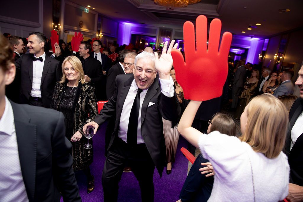 People in a crowd cheering with raised arms. Indoor setting, various skin tones, with smiles and excitement.