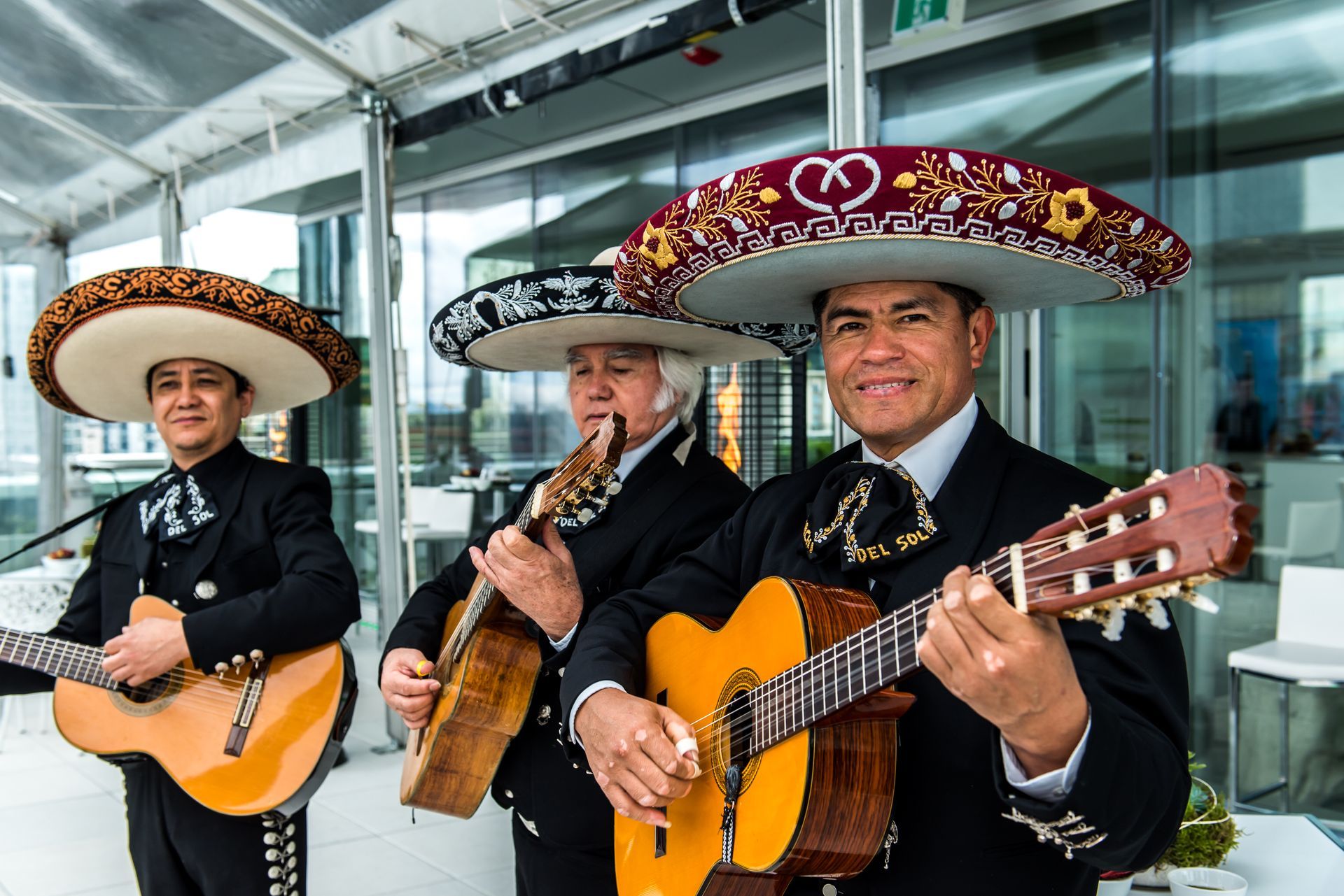 Three mariachi singers are playing guitars and singing into microphones.