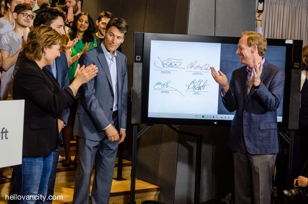 A man in a suit is standing in front of a group of people applauding.