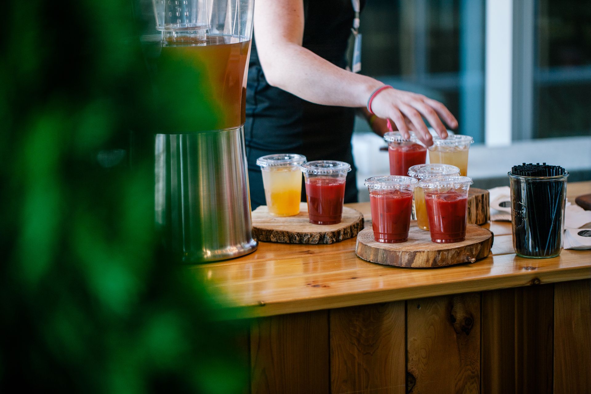 A woman is pouring juice into plastic cups on a wooden table.