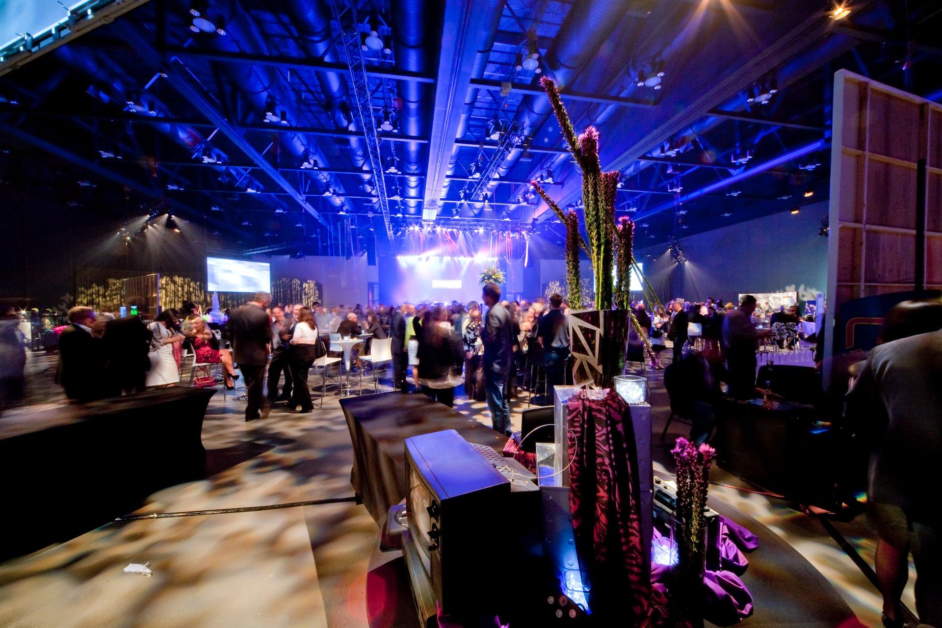 A crowd of people are gathered in a large room with blue lights on the ceiling.