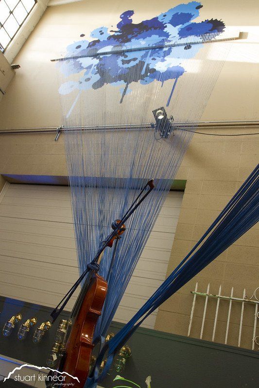 A violin is hanging from the ceiling in front of a painting