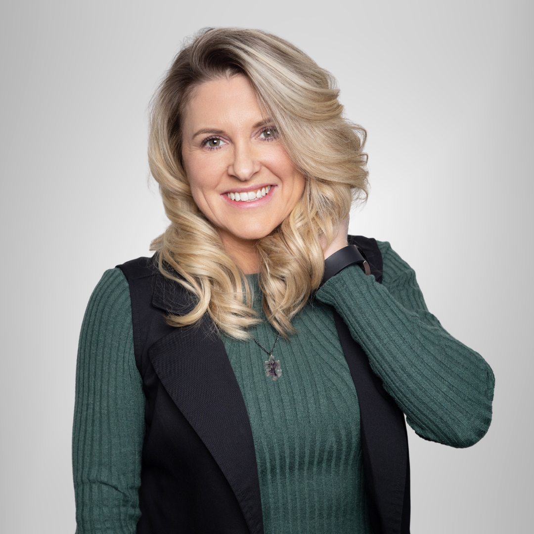 A woman wearing a green sweater and a black vest is smiling.