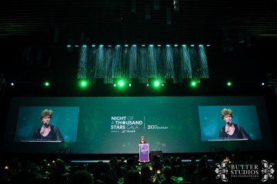 A woman is giving a speech on a stage in front of a large screen.
