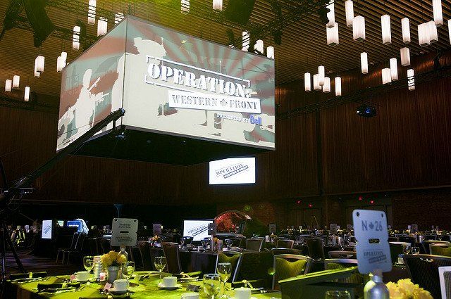 A large screen is hanging from the ceiling above a dining room